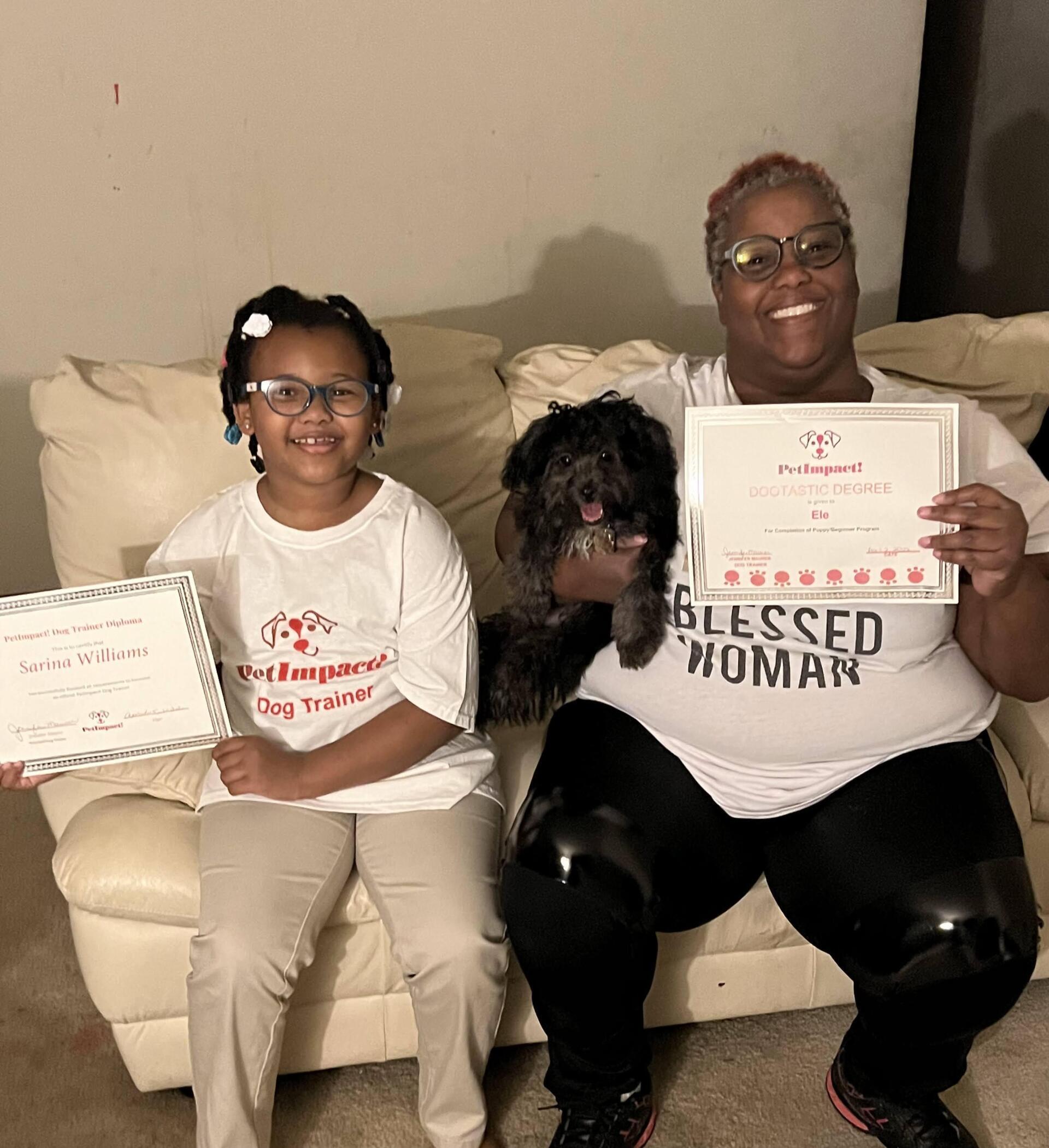 Woman and child on a couch, holding certificates with a small dog between them.