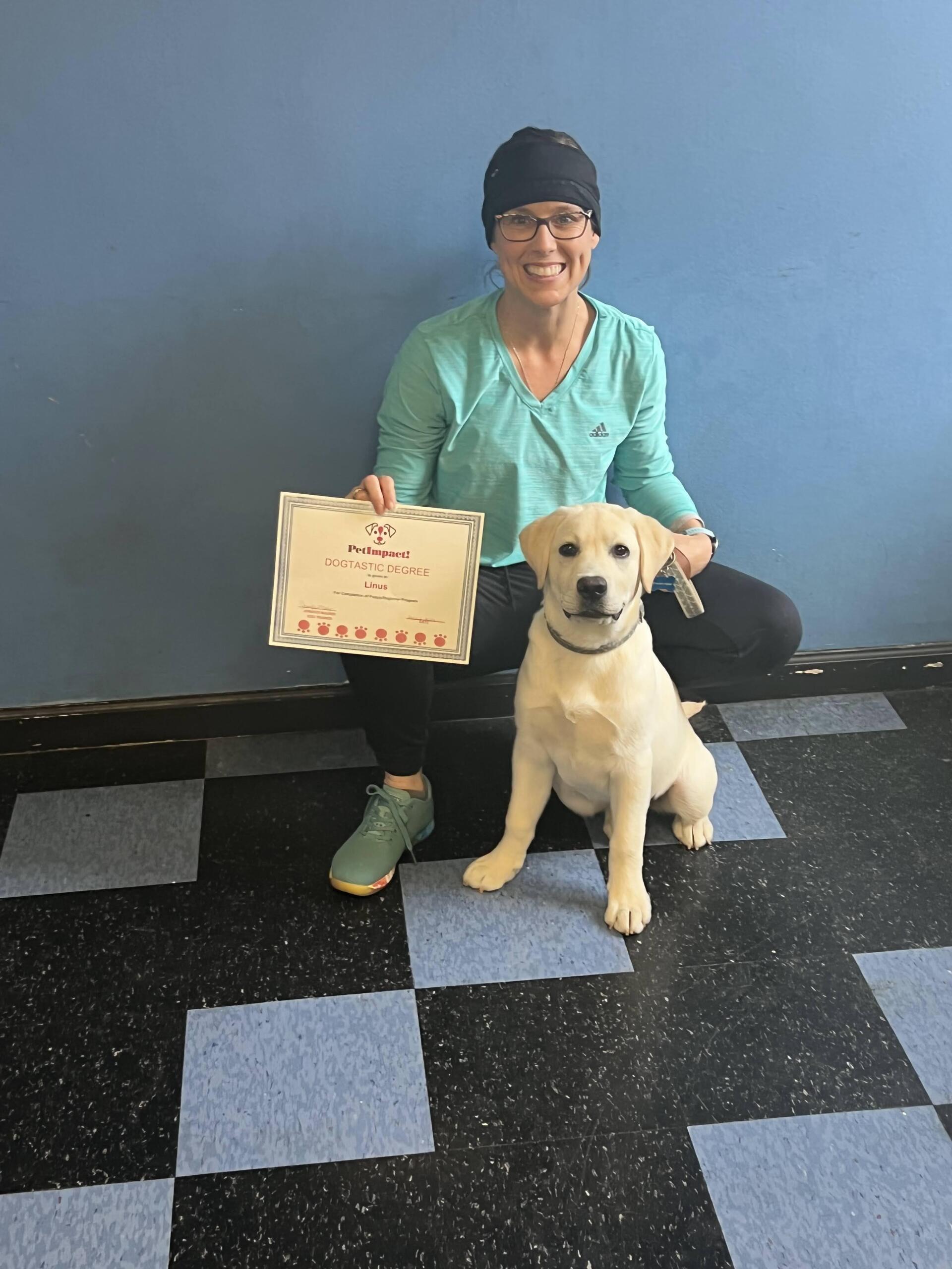 Woman and puppy with certificate; blue wall backdrop, checkered floor.