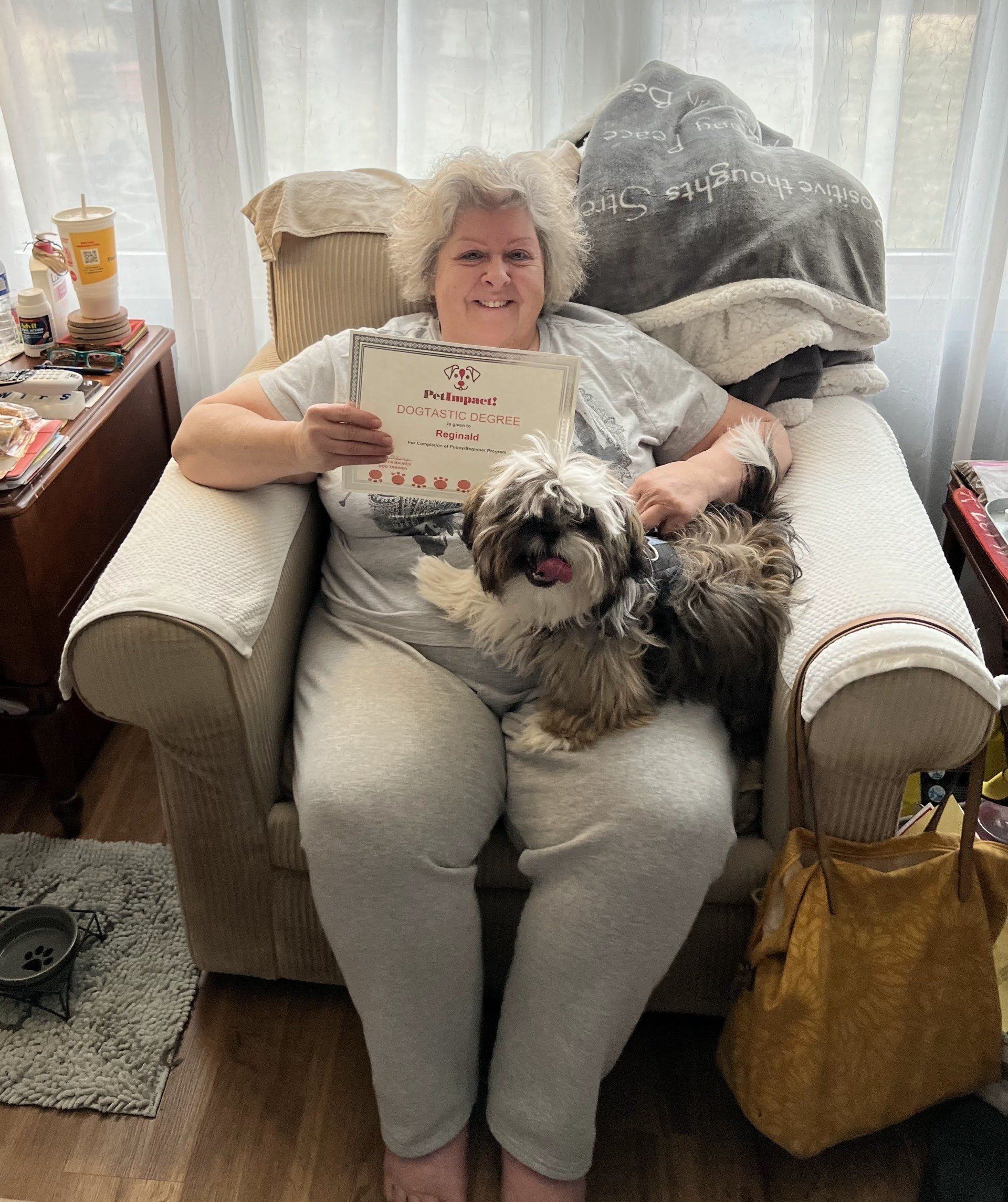 Woman holding a sign and a dog, sitting in a chair, with a window in the background.
