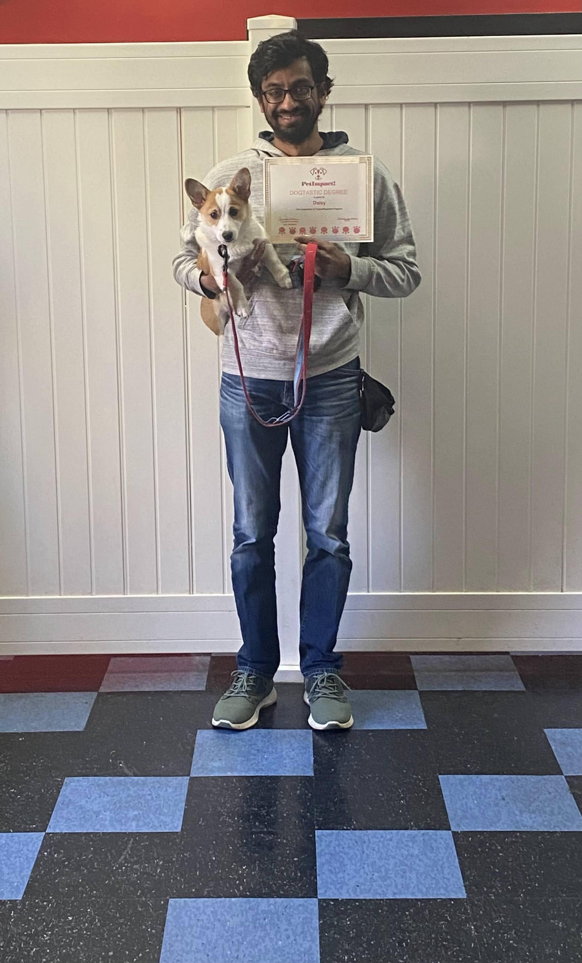 Person holding dog and certificate, posing in room with checkered floor and white paneling.