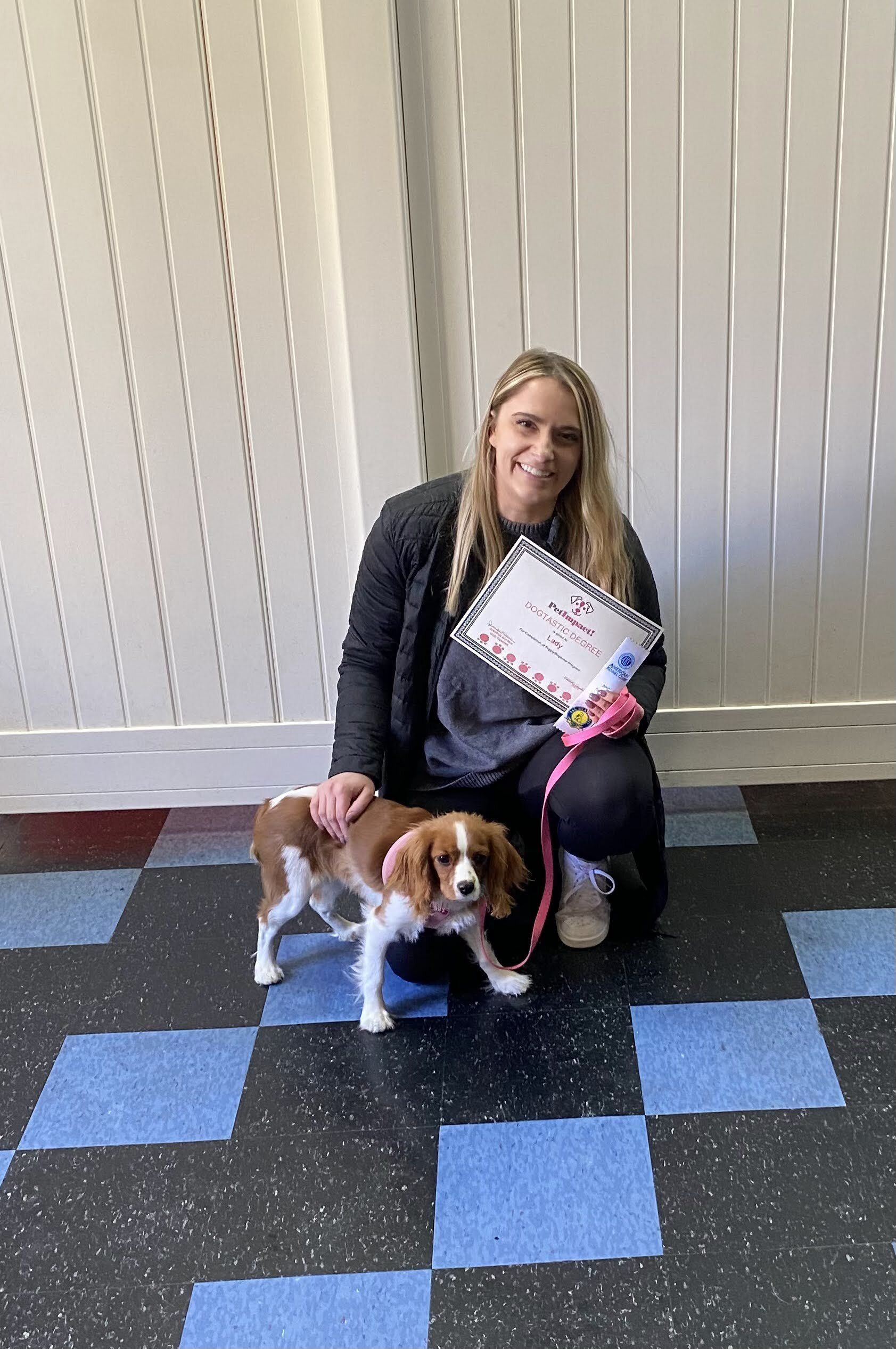 Woman kneeling, petting a Cavalier King Charles Spaniel. Both are in a checkered hallway.