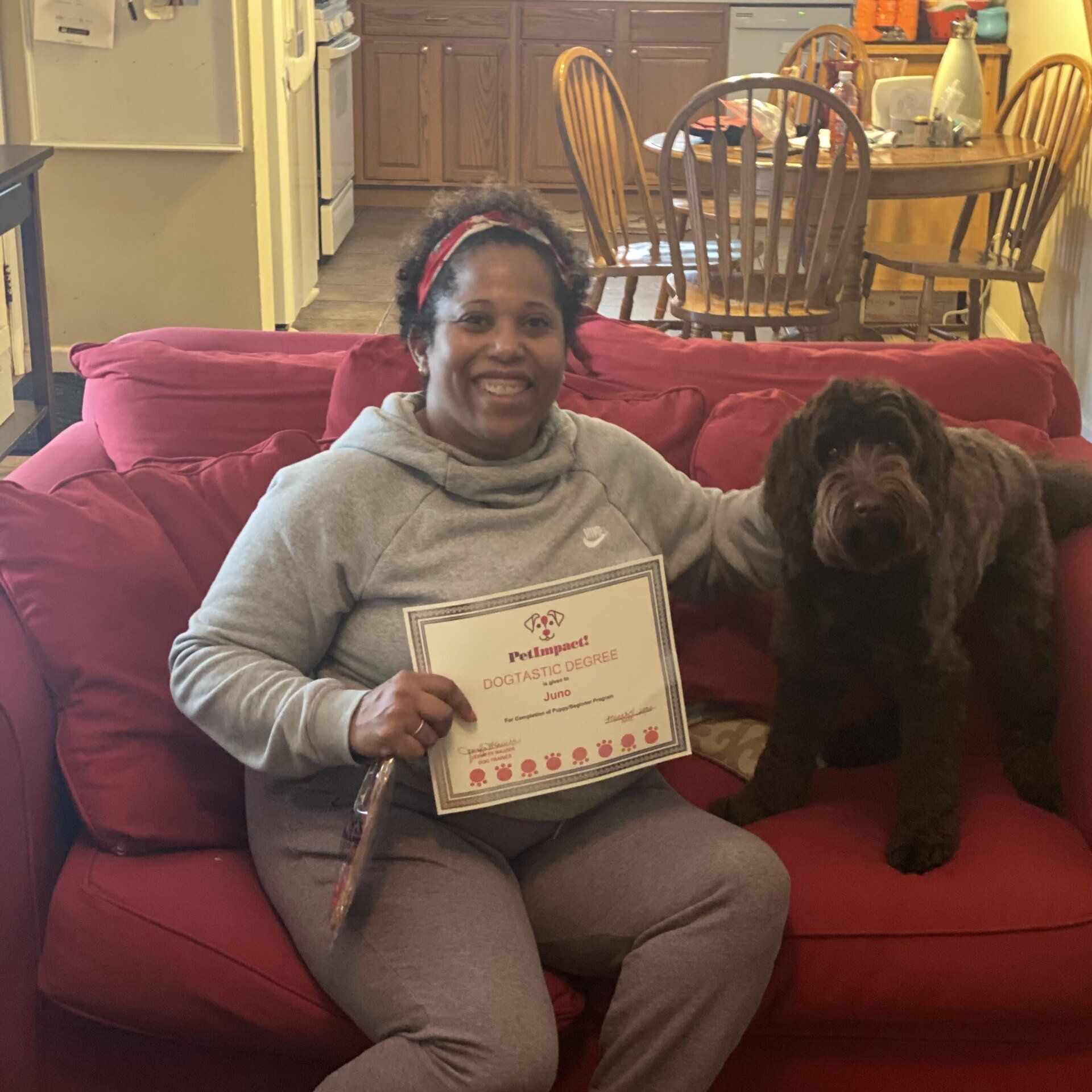 Woman and brown dog on red couch, holding certificate in a home setting.