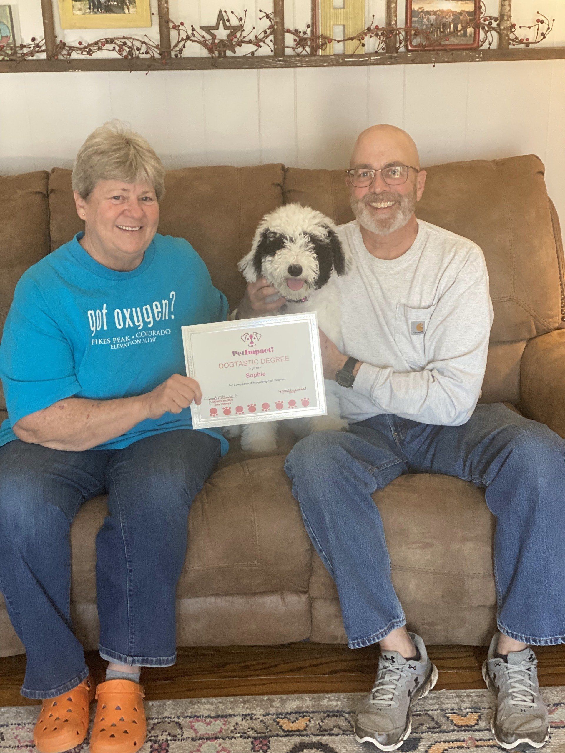 Two people and a dog seated on a couch holding a certificate.