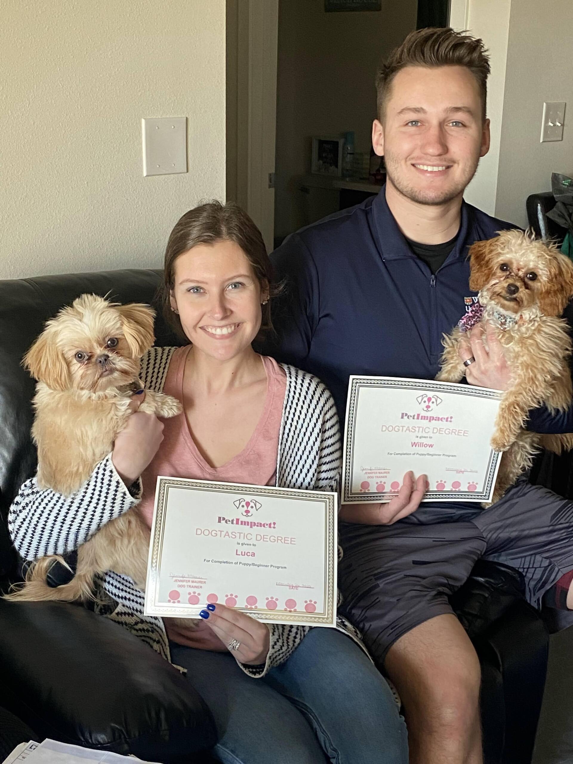 Couple on couch holding dogs and certificates.