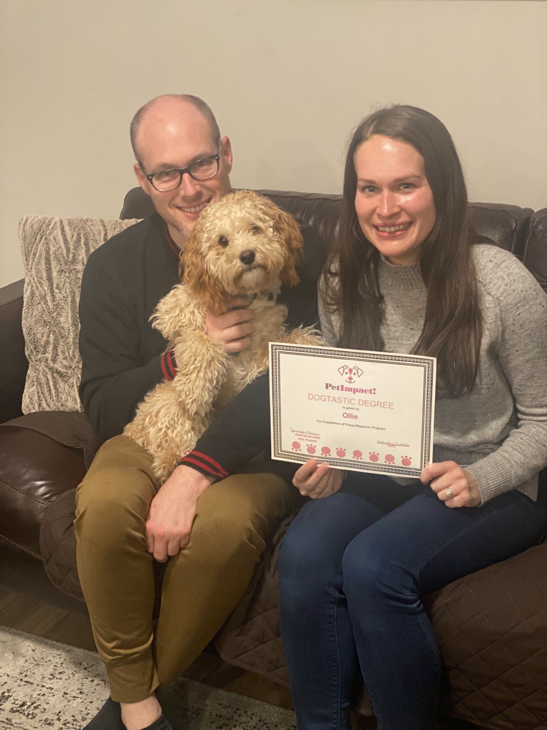 Couple on a couch with a small dog, holding a framed certificate.