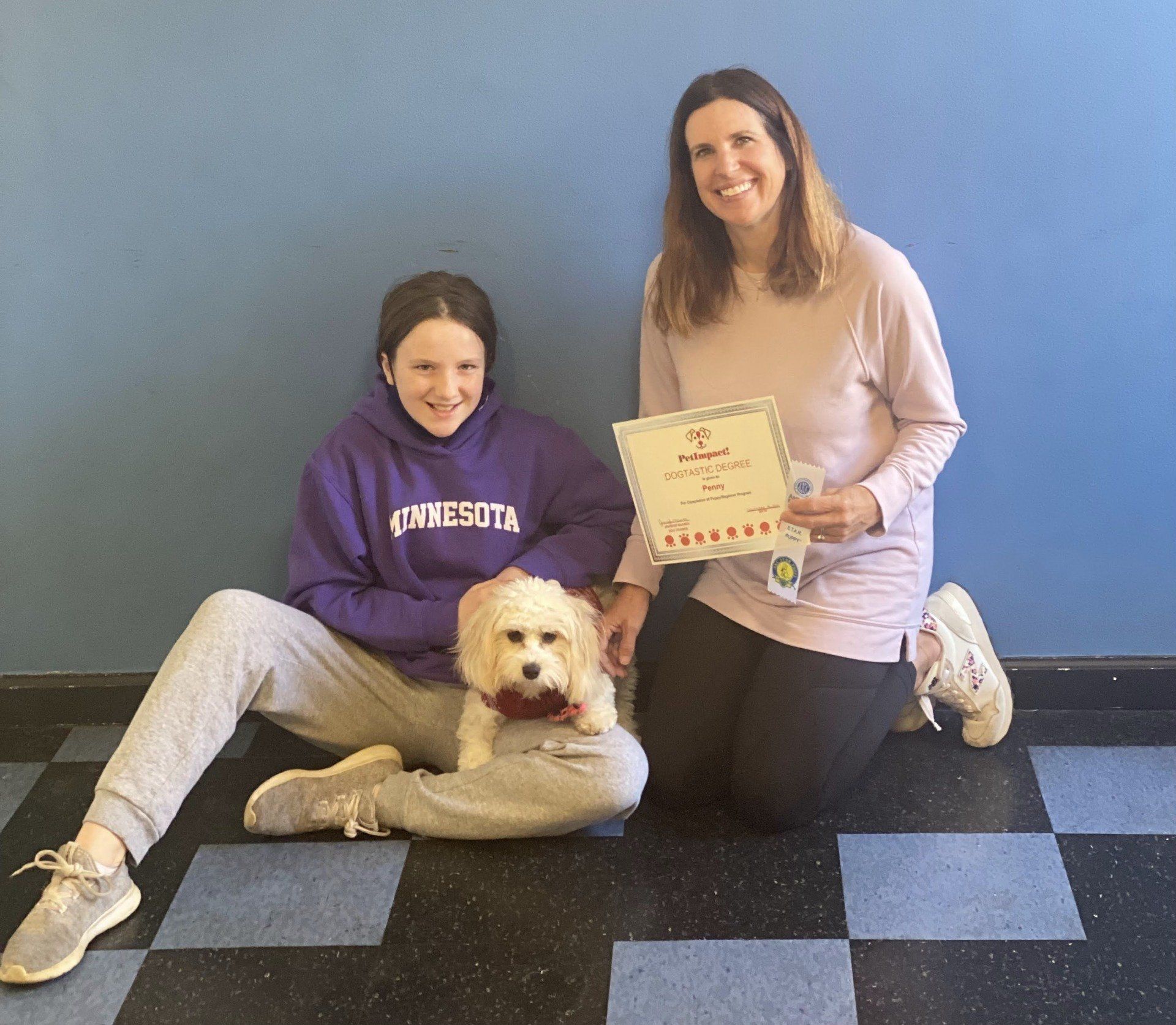 Girl and woman with dog by blue wall; holding award.