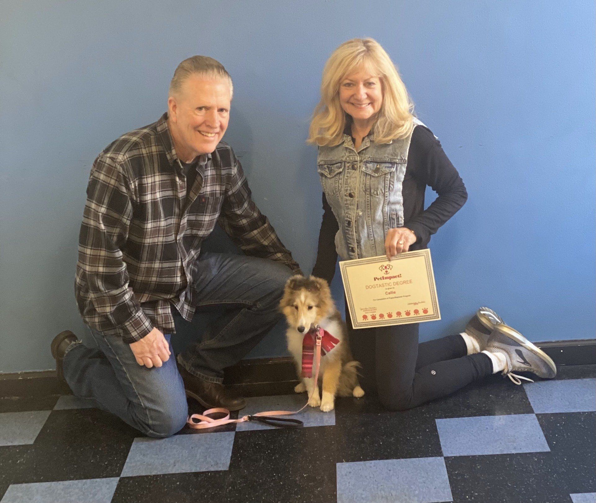 Man, woman, and puppy with a certificate, posing in front of a blue wall.