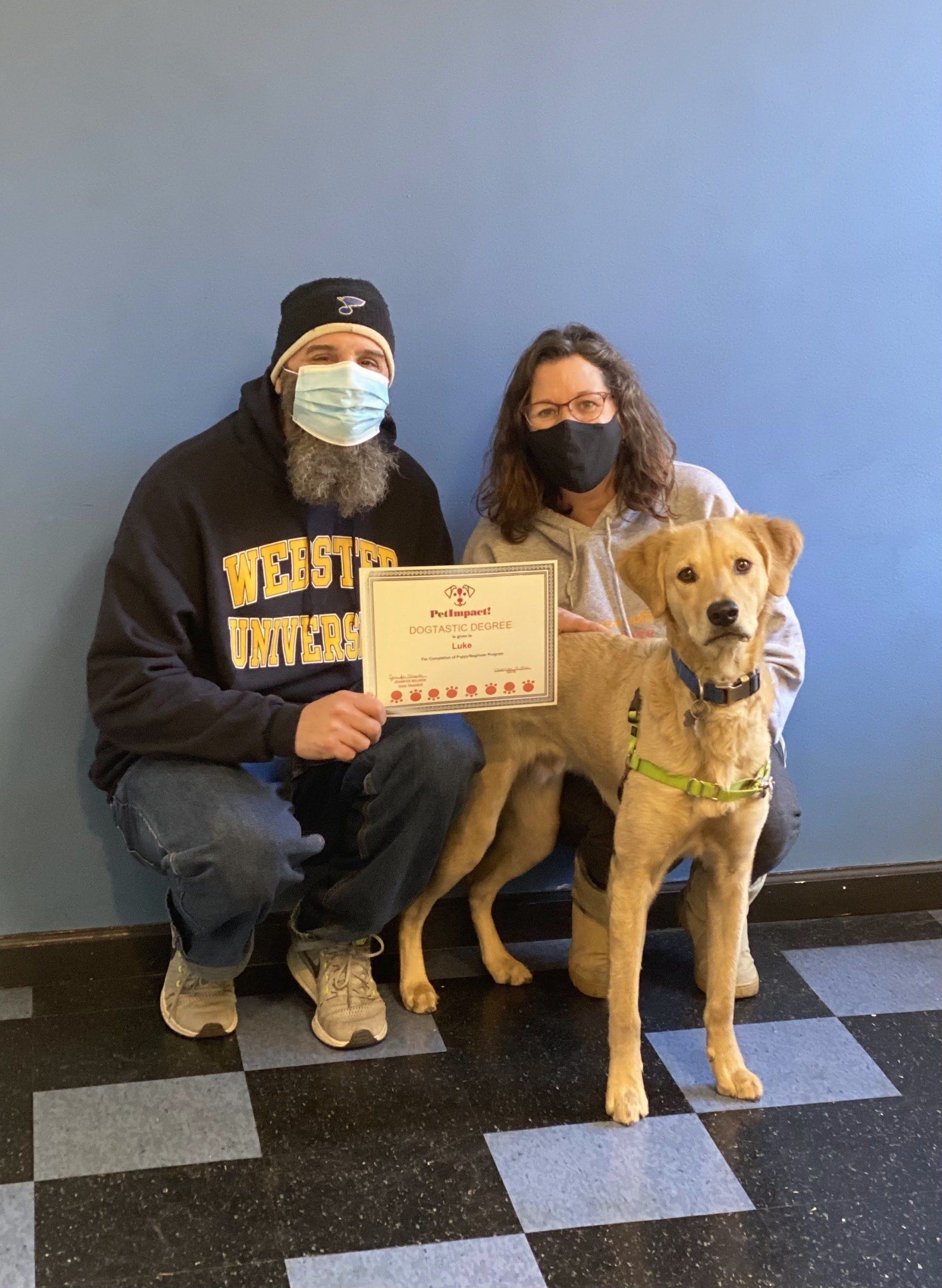 Couple with dog hold adoption certificate, posing against a blue wall.