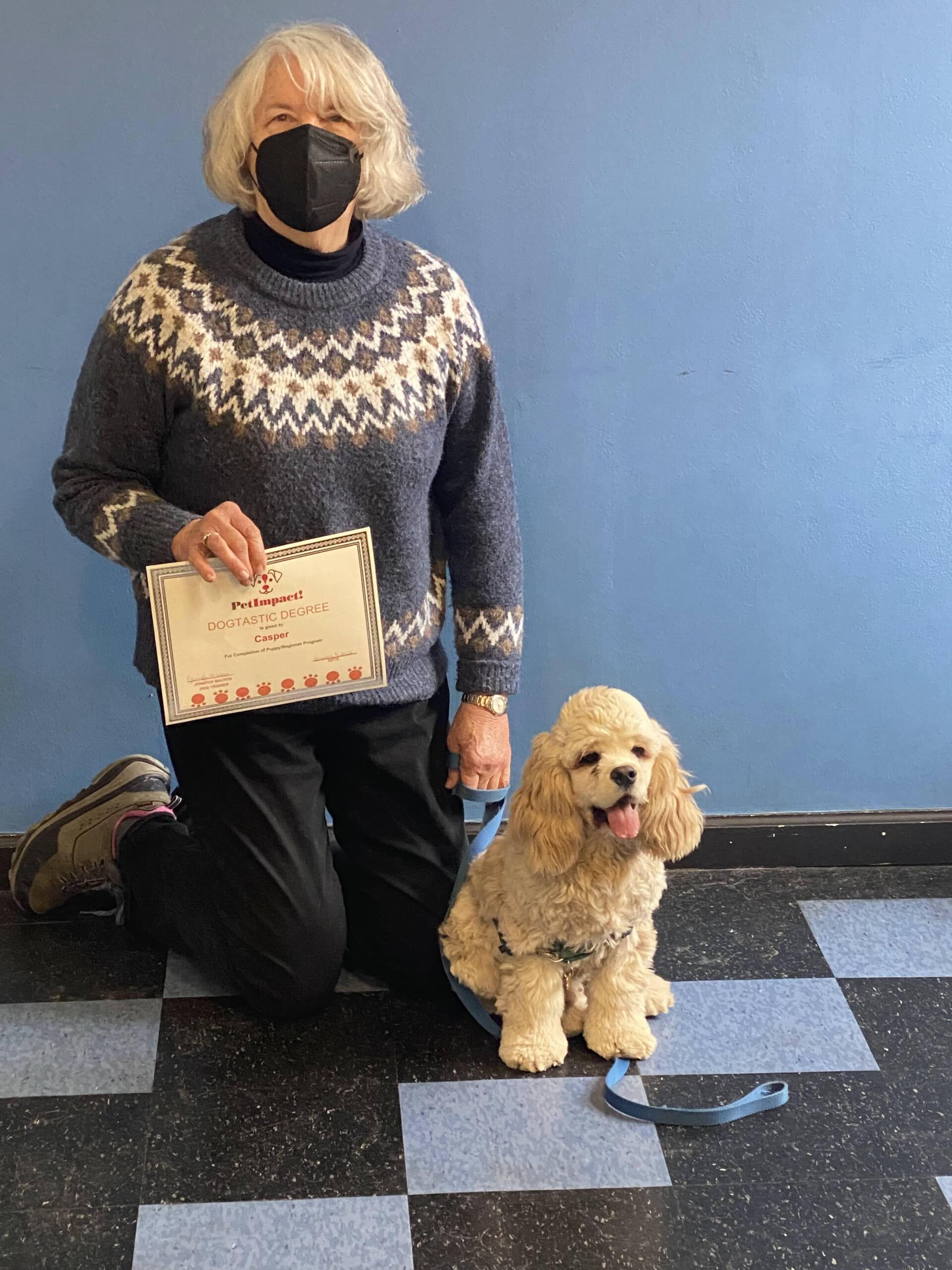 Woman kneeling with poodle, holding a card; blue wall and checkered floor.