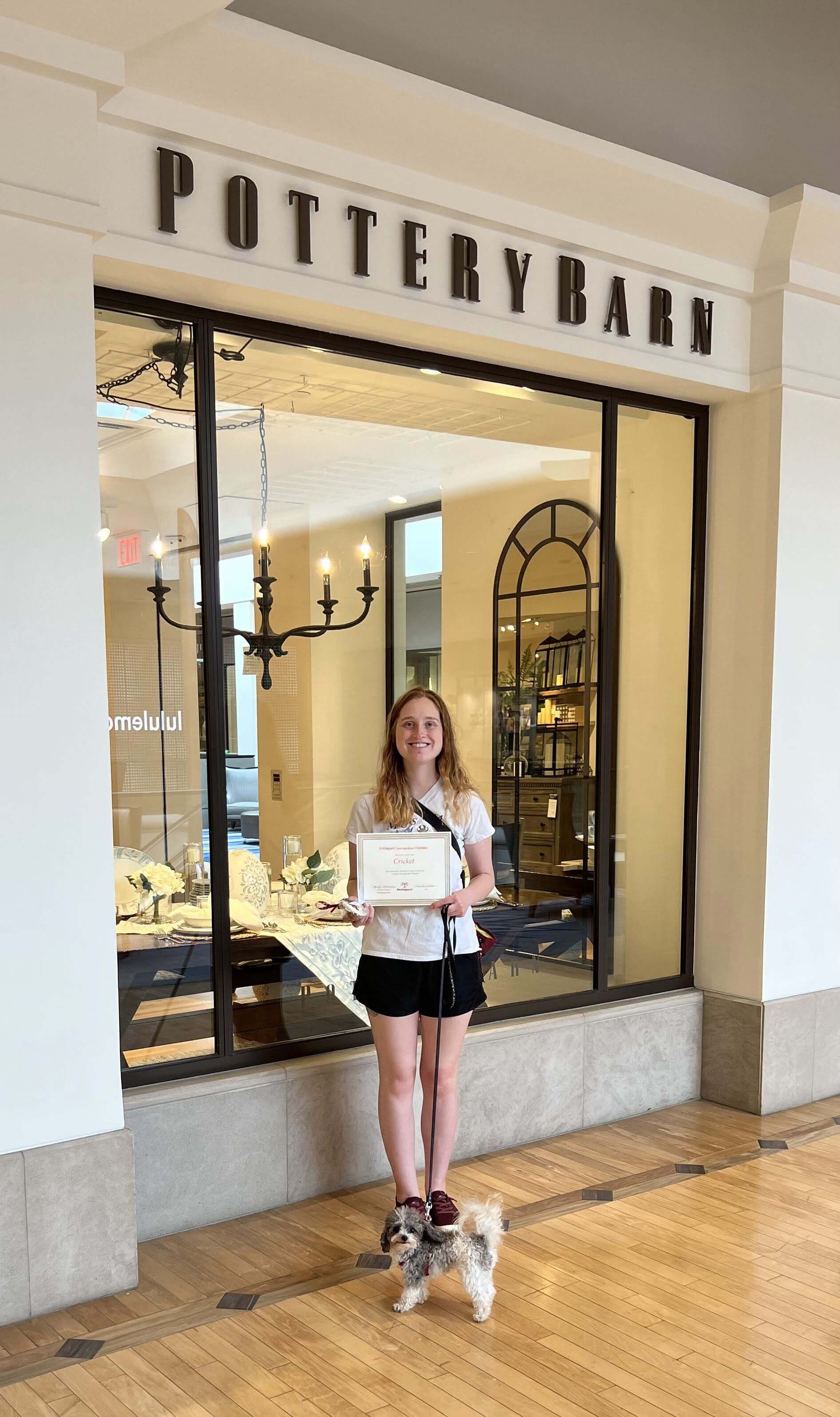 Teenager and small dog in front of Pottery Barn store, holding a framed certificate.