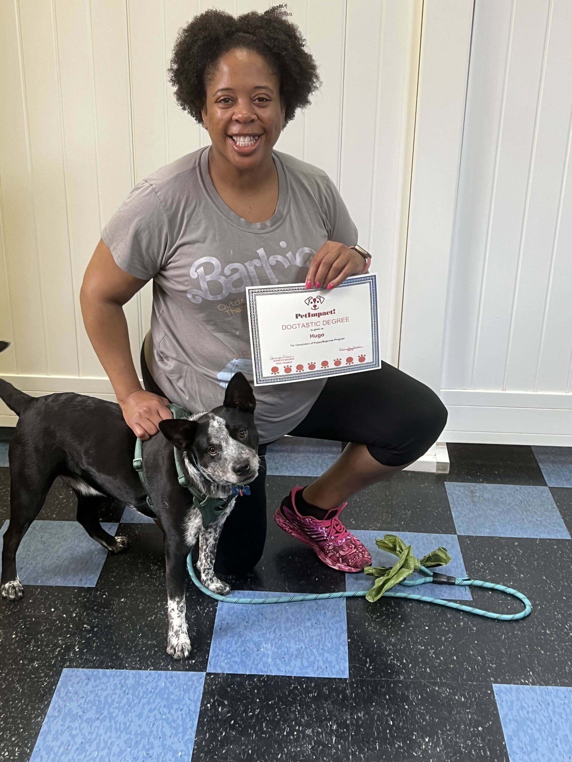 Woman kneels next to a dog, holding a certificate. The dog is on a leash and looking at the camera.