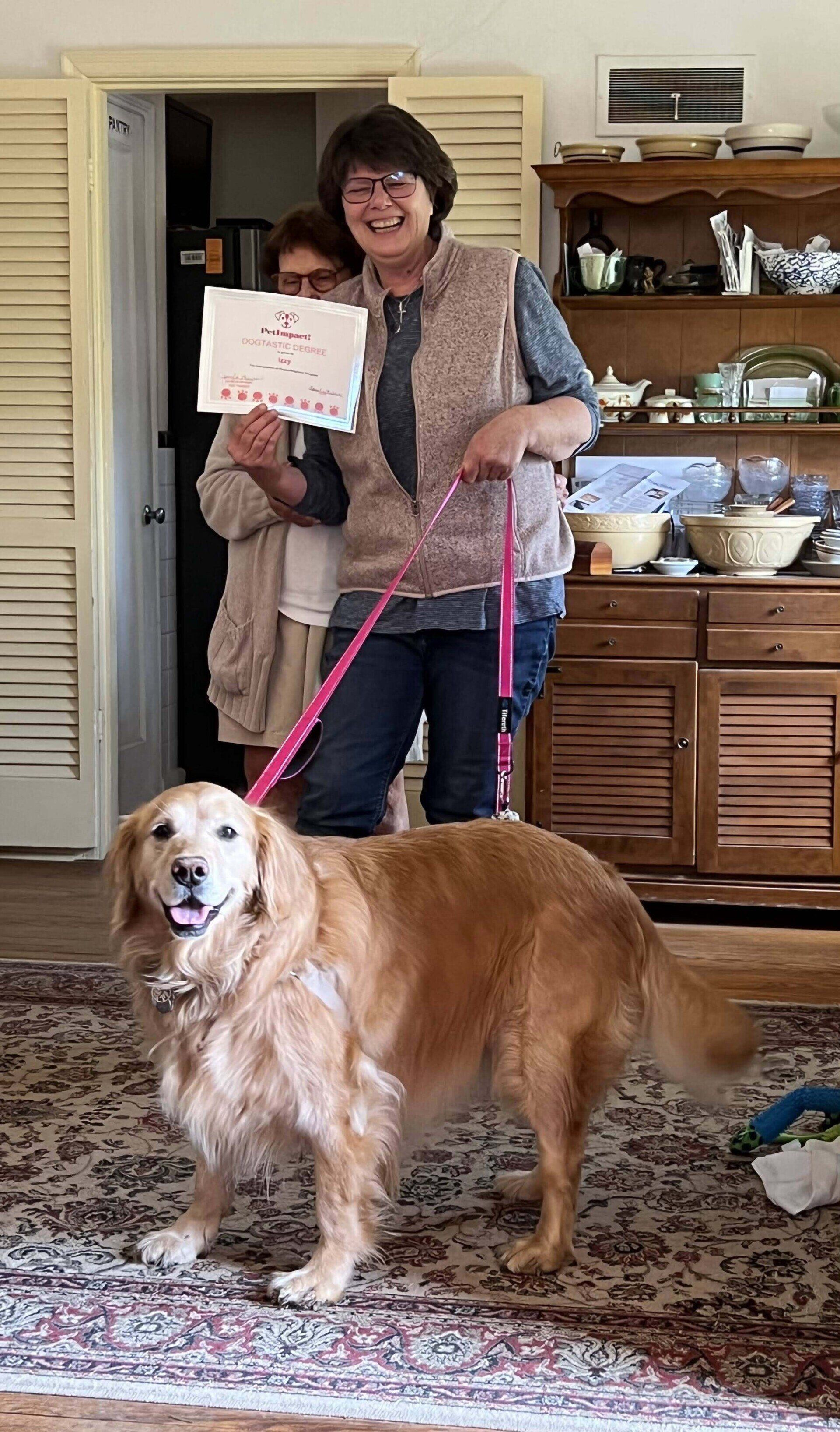 Golden retriever on leash with two women in a home; one woman holds a sign.