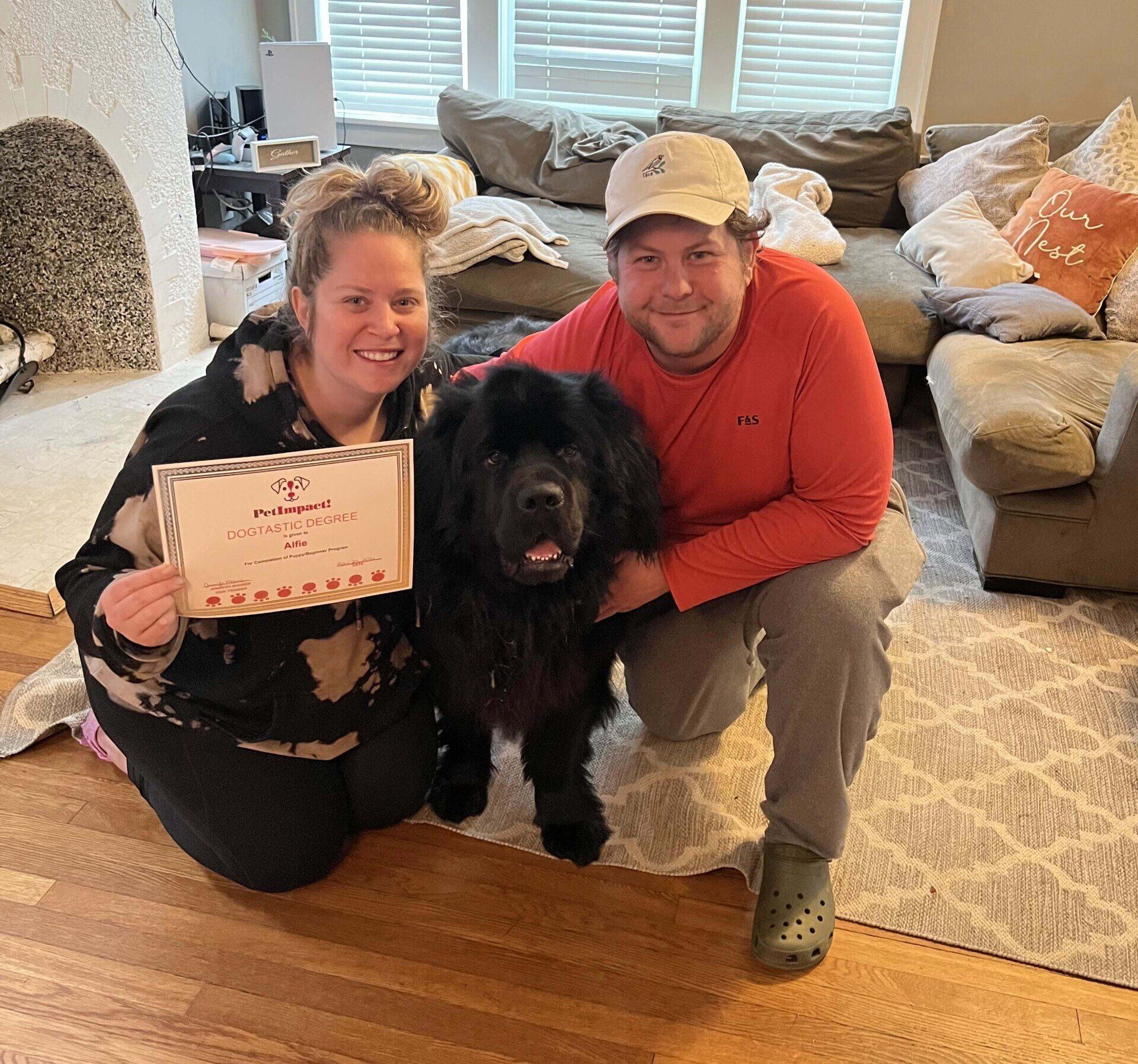 Couple with large black dog holding certificate, posing in a living room.