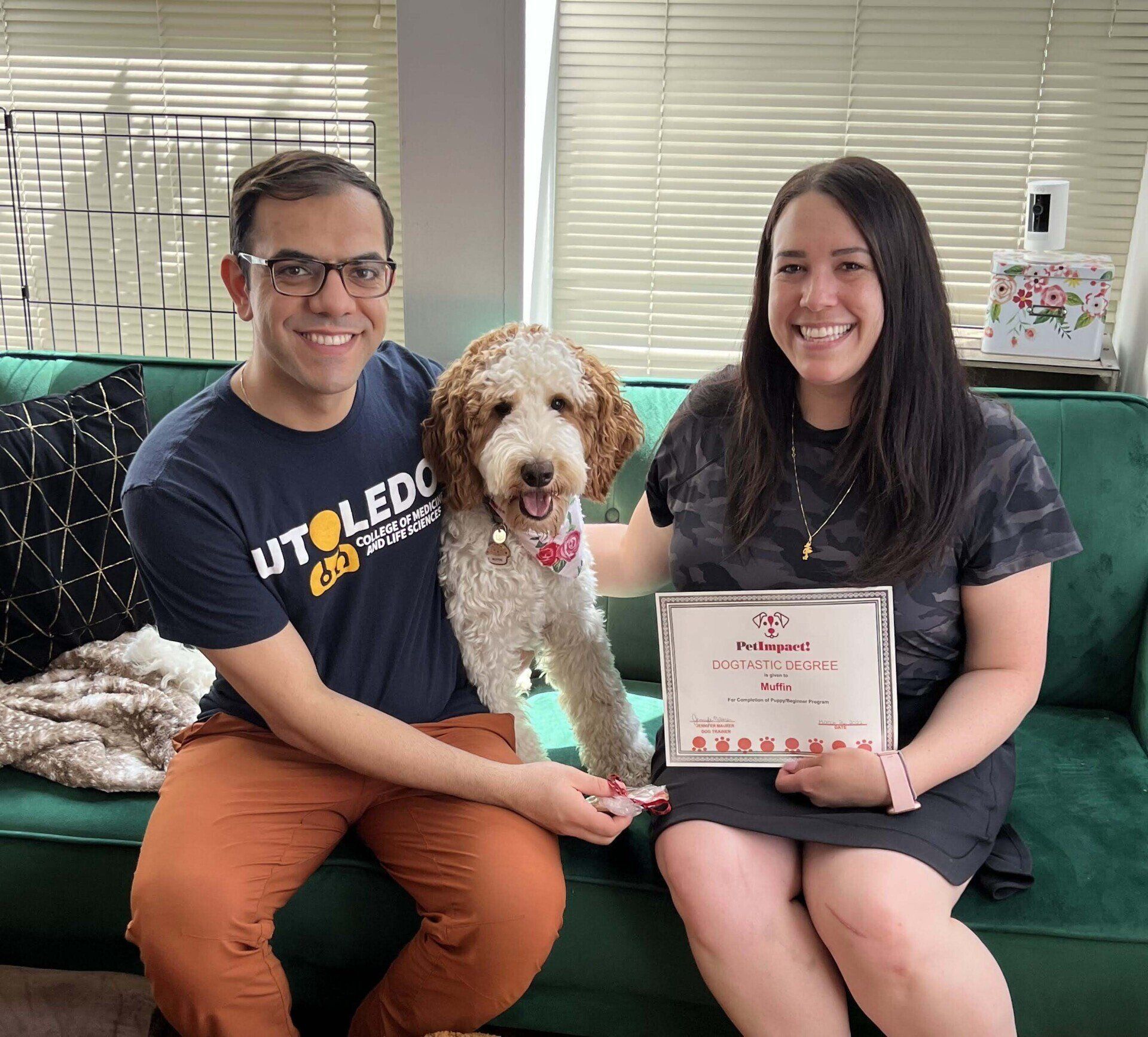 A couple and a dog on a green couch holding a certificate.