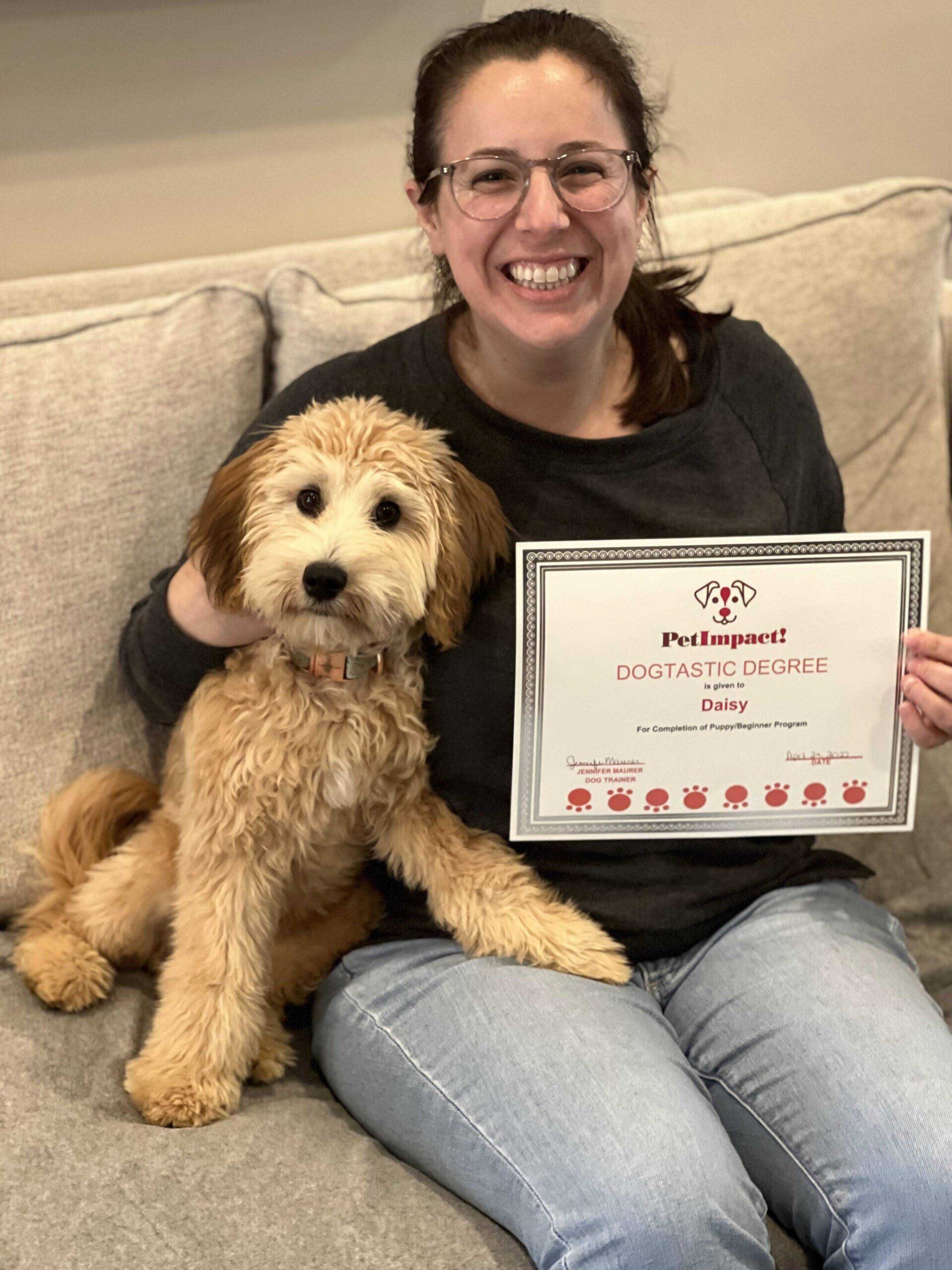Woman with a goldendoodle puppy, smiling, holding a certificate on a couch.