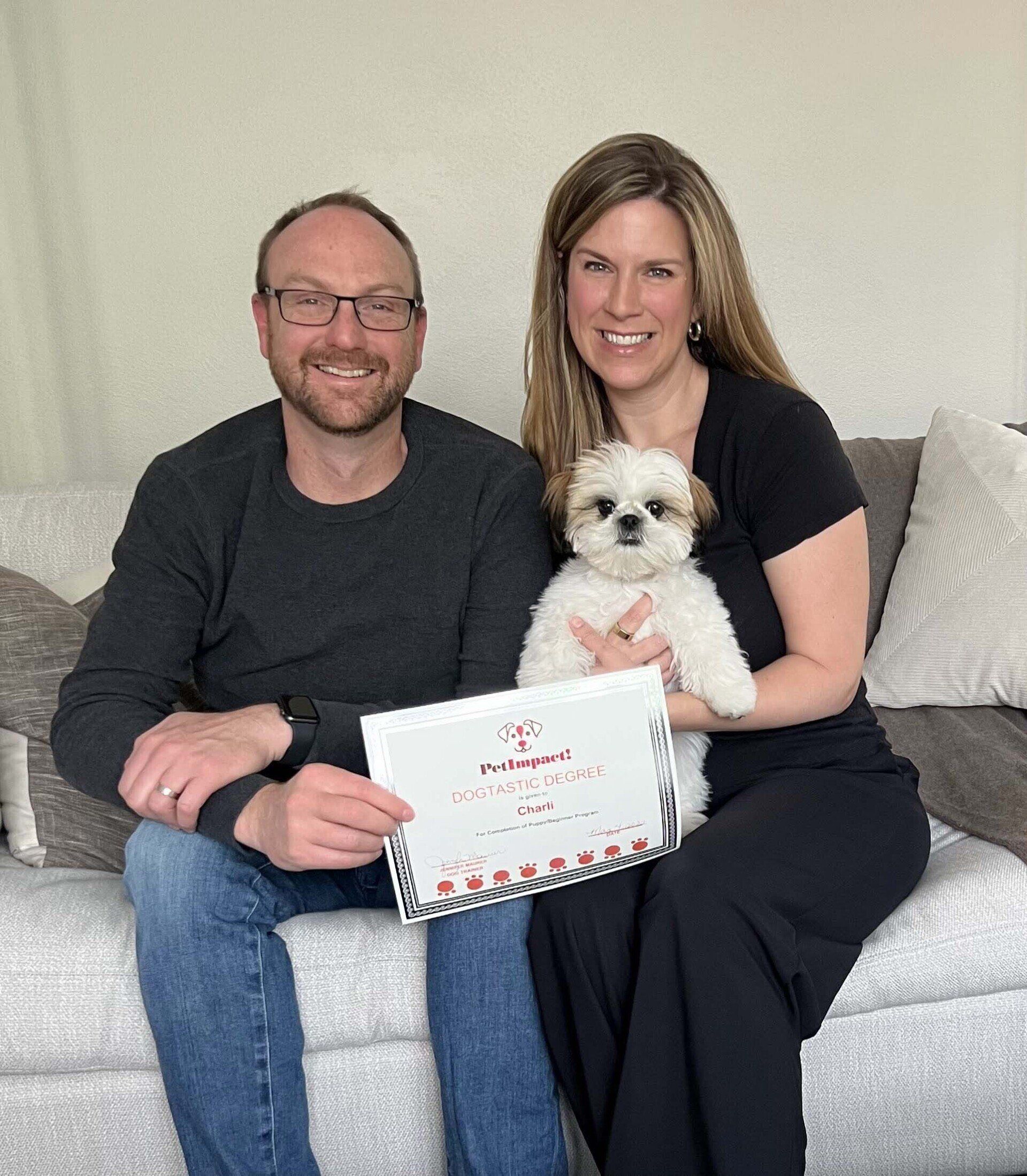 Couple with a small dog holding a certificate, smiling on a couch.