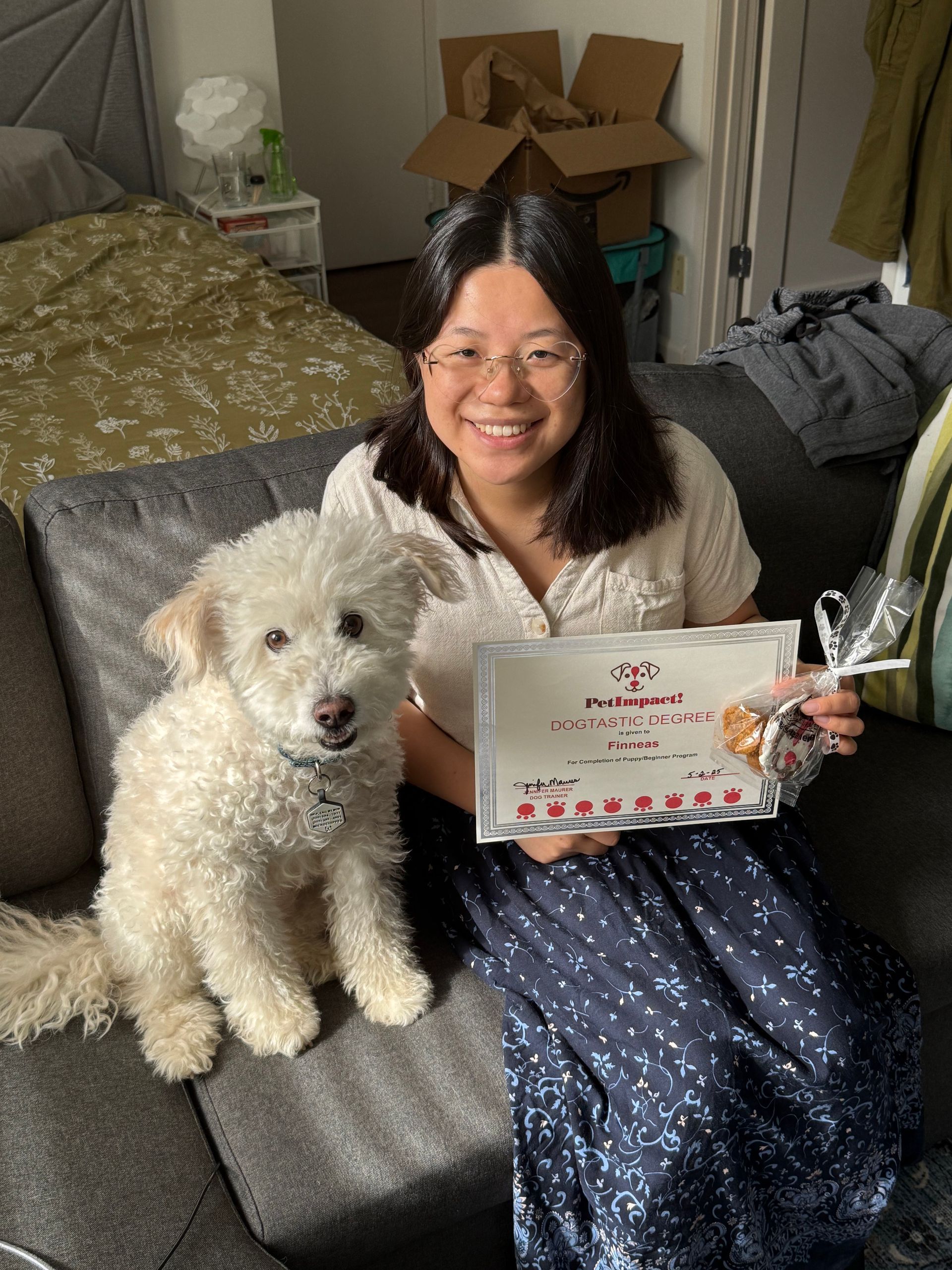 A woman is sitting on a couch with a white dog and holding a certificate.