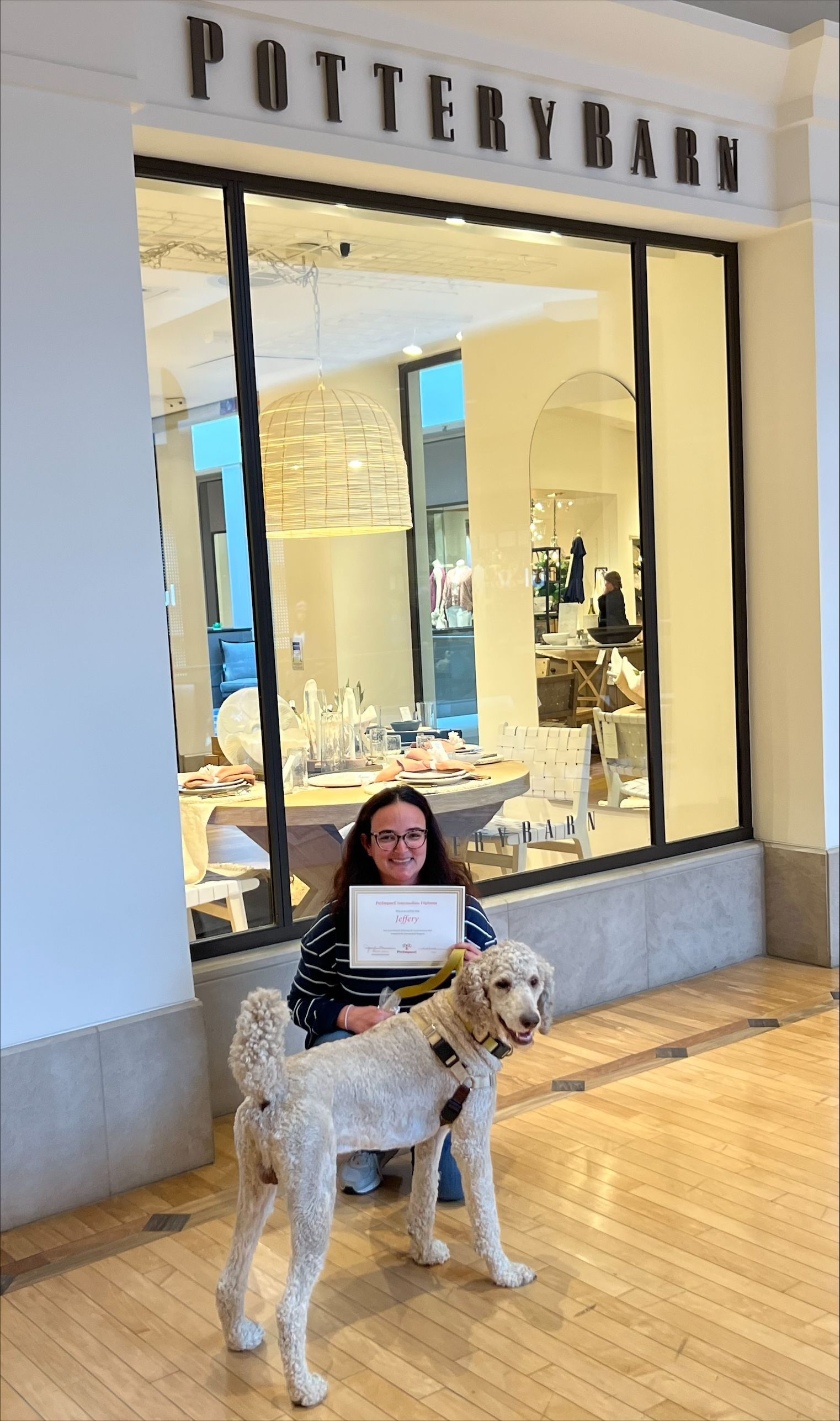 Woman and dog pose in front of Pottery Barn store. Woman holds a framed certificate.