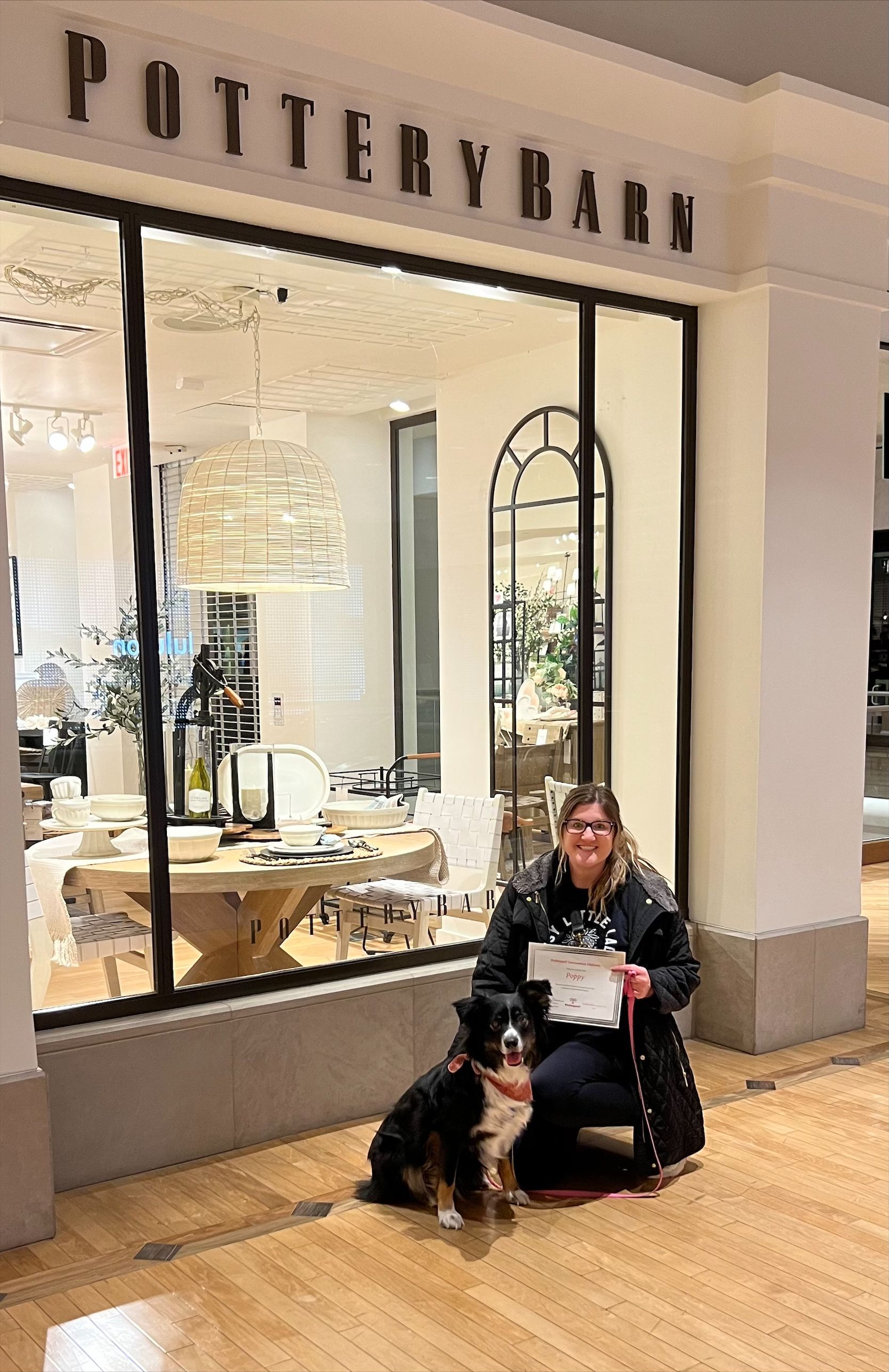 Woman and dog in front of a Pottery Barn store display. The woman holds a document.