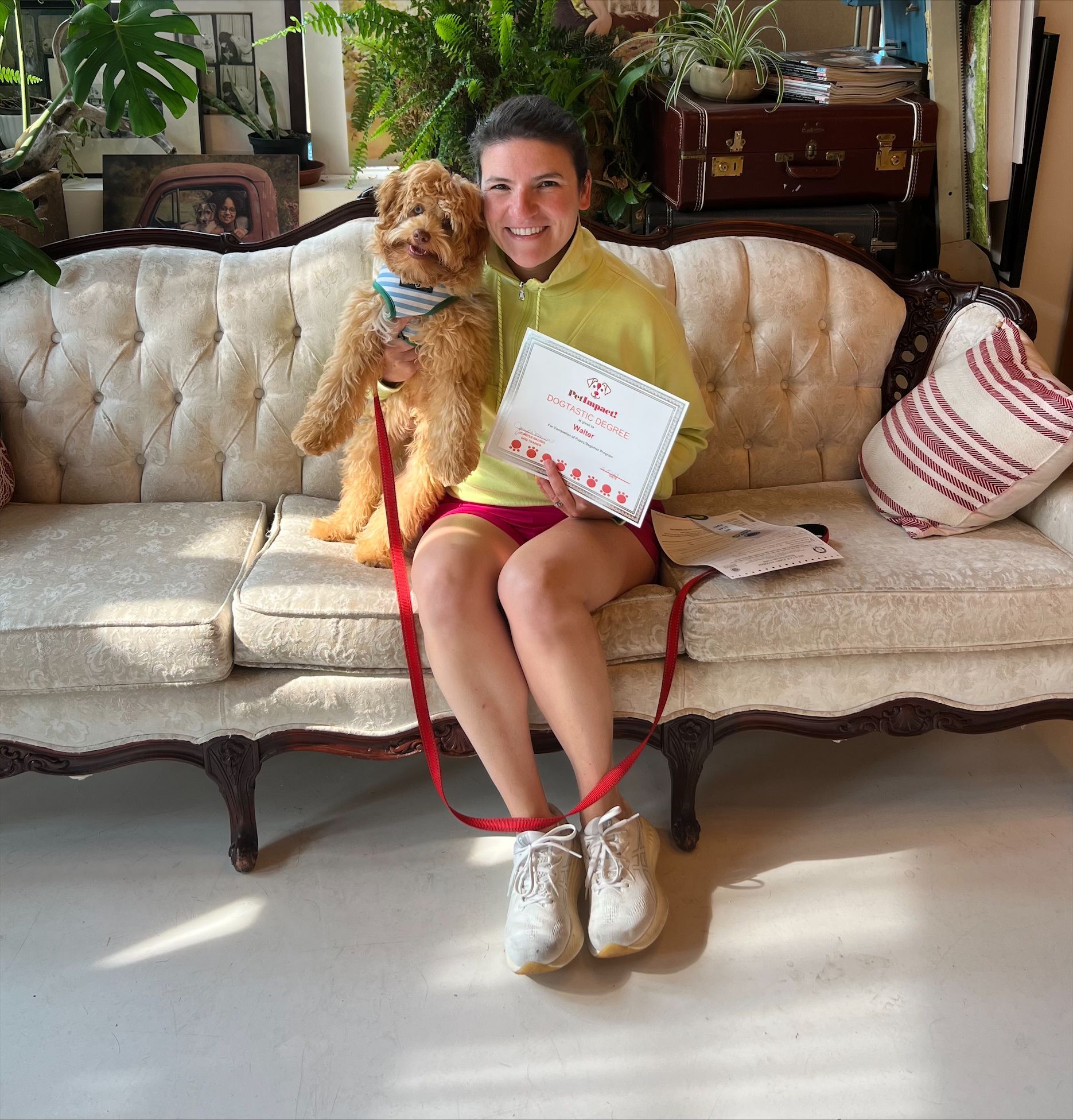 Woman in yellow hoodie sits on couch with dog, holding a certificate.