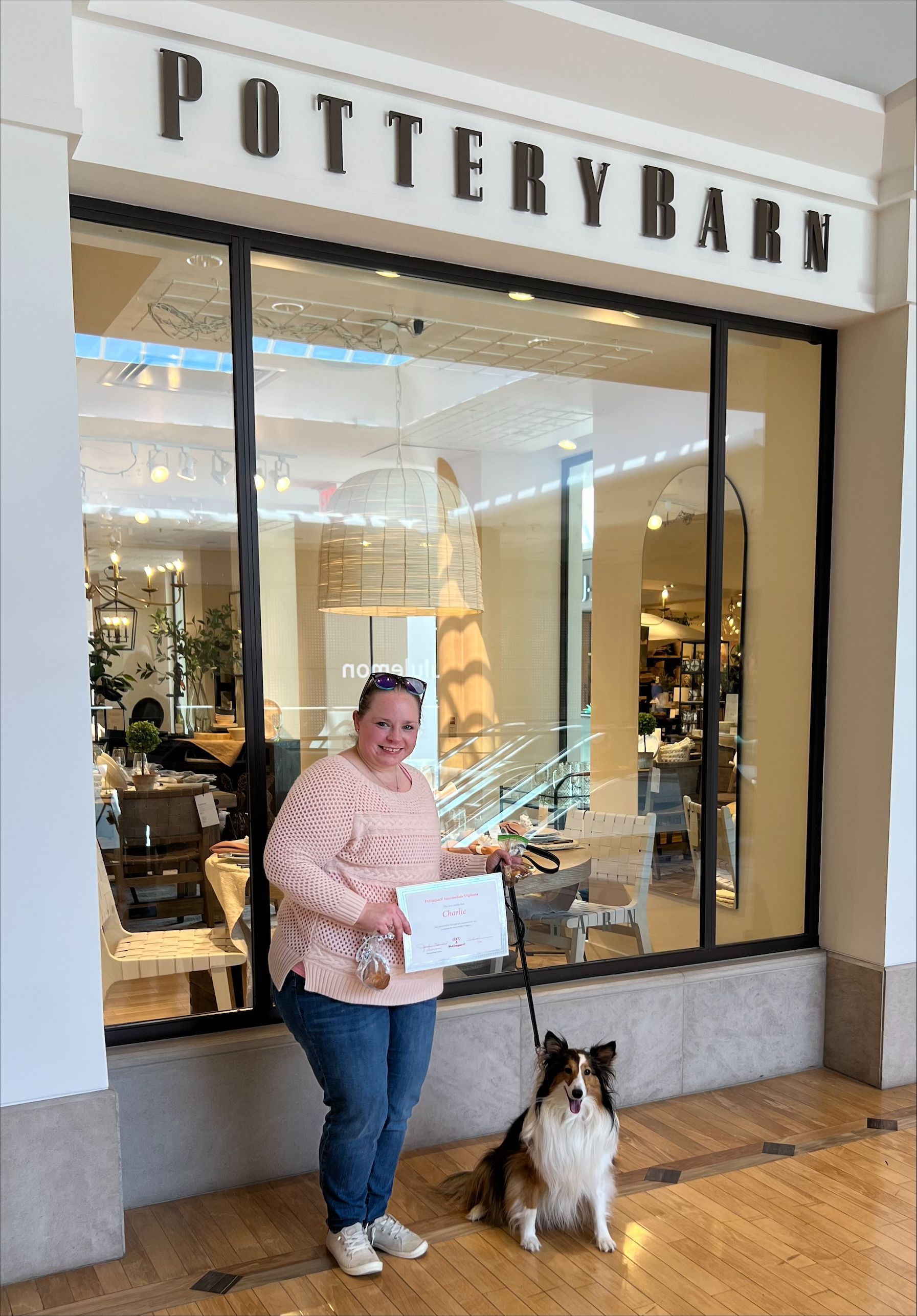 Woman with dog in front of Pottery Barn store, holding a paper.