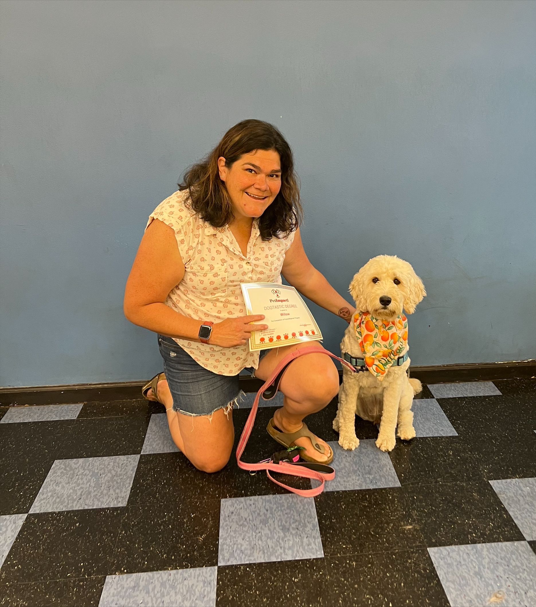 Woman kneeling with a fluffy, light-colored dog on a tiled floor. Both are smiling.