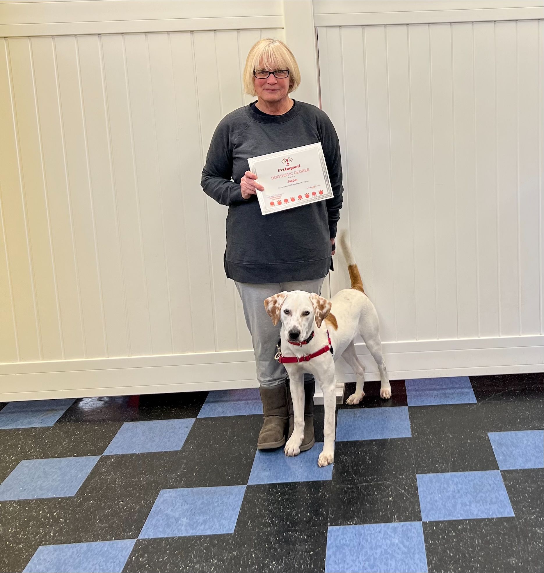 Woman holding a certificate stands with a white and brown dog in front of a white wall.