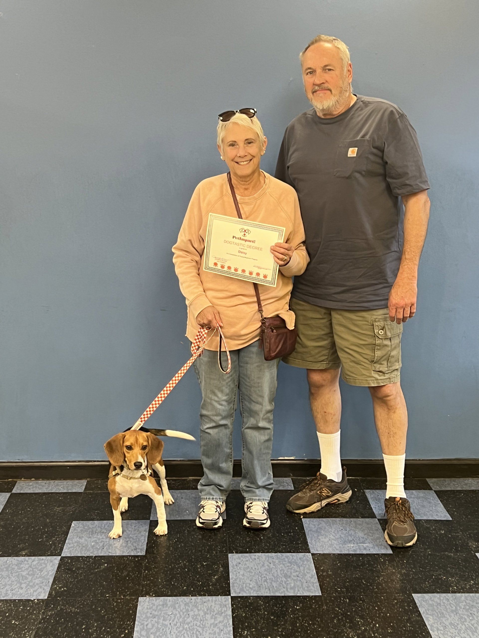 A woman and man with a beagle, the woman holding a certificate.