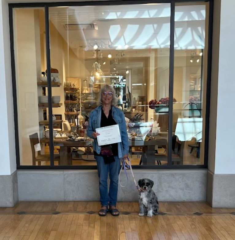 A woman standing next to a small dog holding a certificate