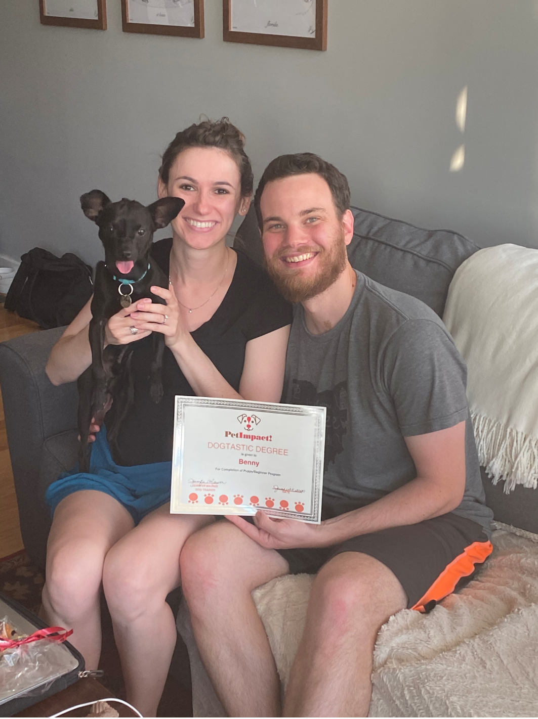 Couple and black dog sit, holding a signed document; smiling.