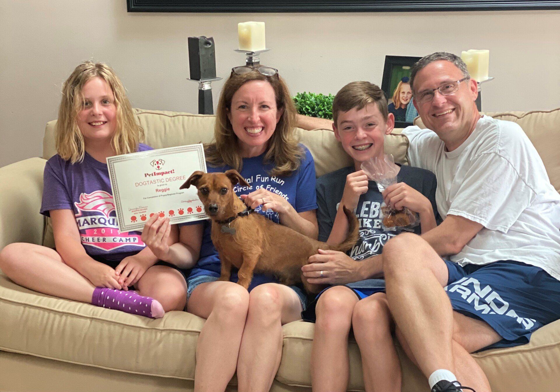 Family of four and a dog on a couch, holding a certificate.