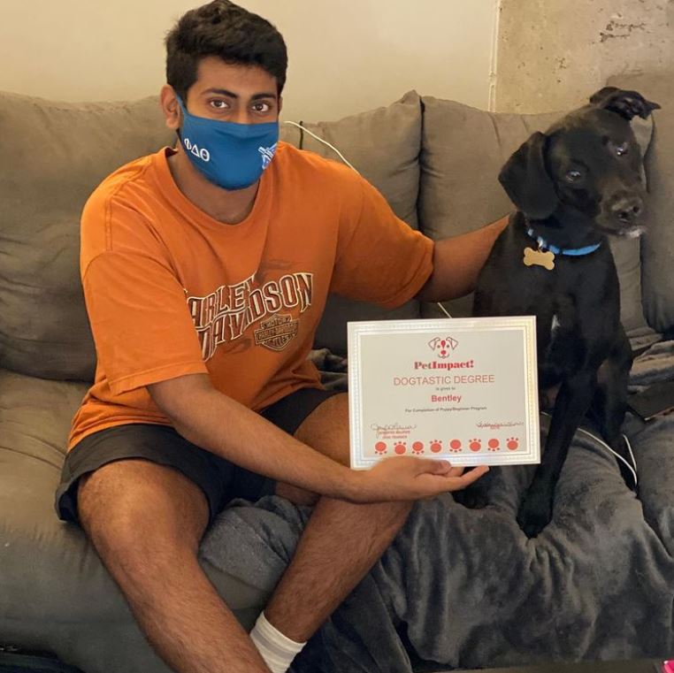 Man in orange shirt with dog, holding a certificate. They are sitting on a couch. The dog is black.