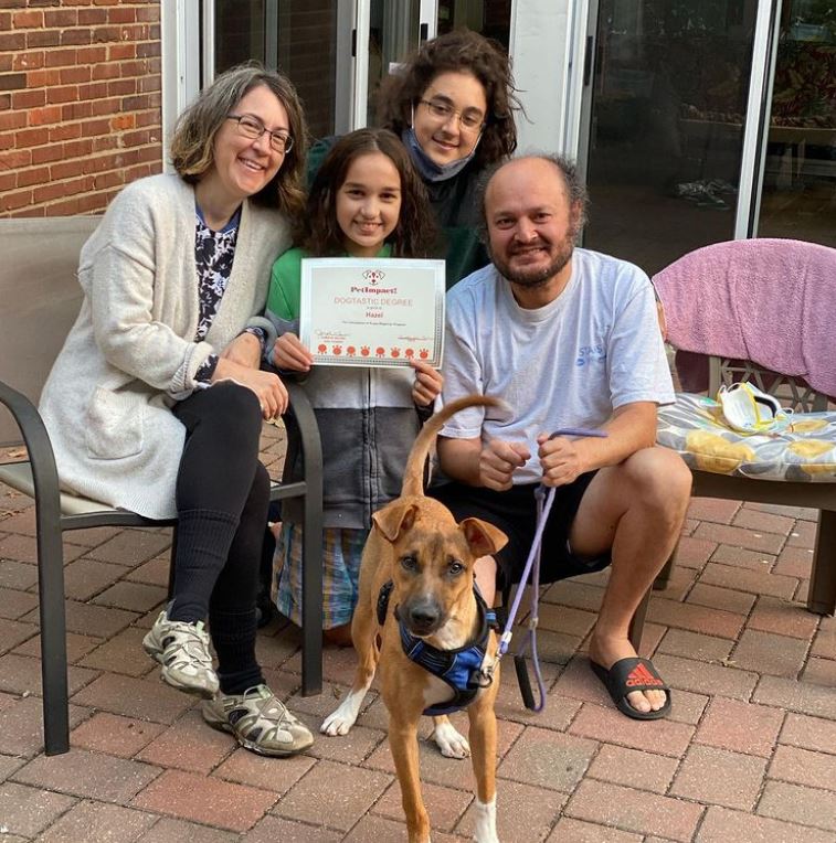 Family and dog pose on patio, holding a certificate.