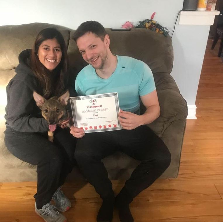 Two people and a dog seated on a couch, holding an award. Smiling.