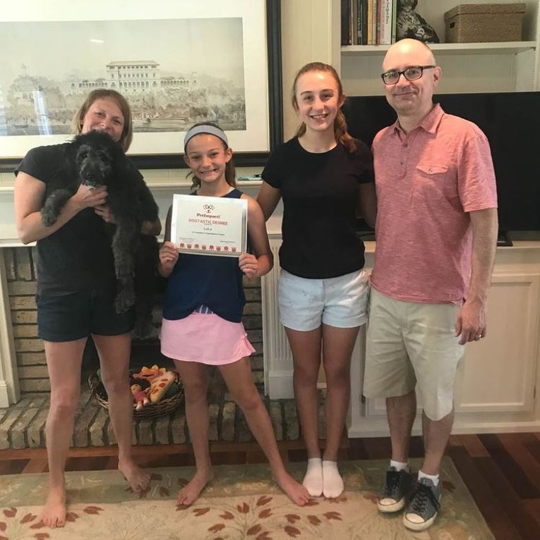 Family with dog, indoors, celebrating a certificate. The young girl holds a certificate; all smile.