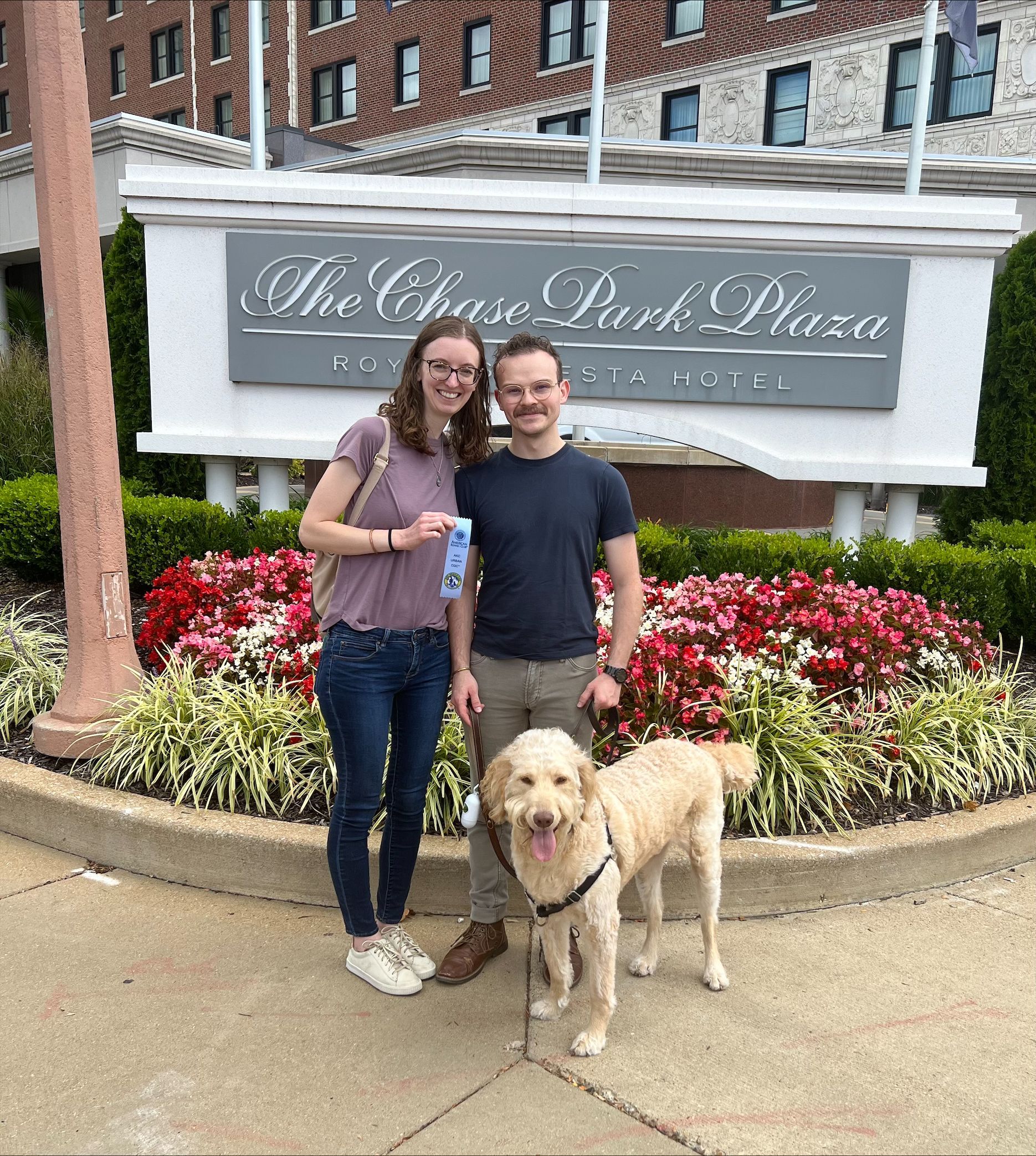 A couple stands with a golden doodle in front of The Chase Park Plaza hotel.