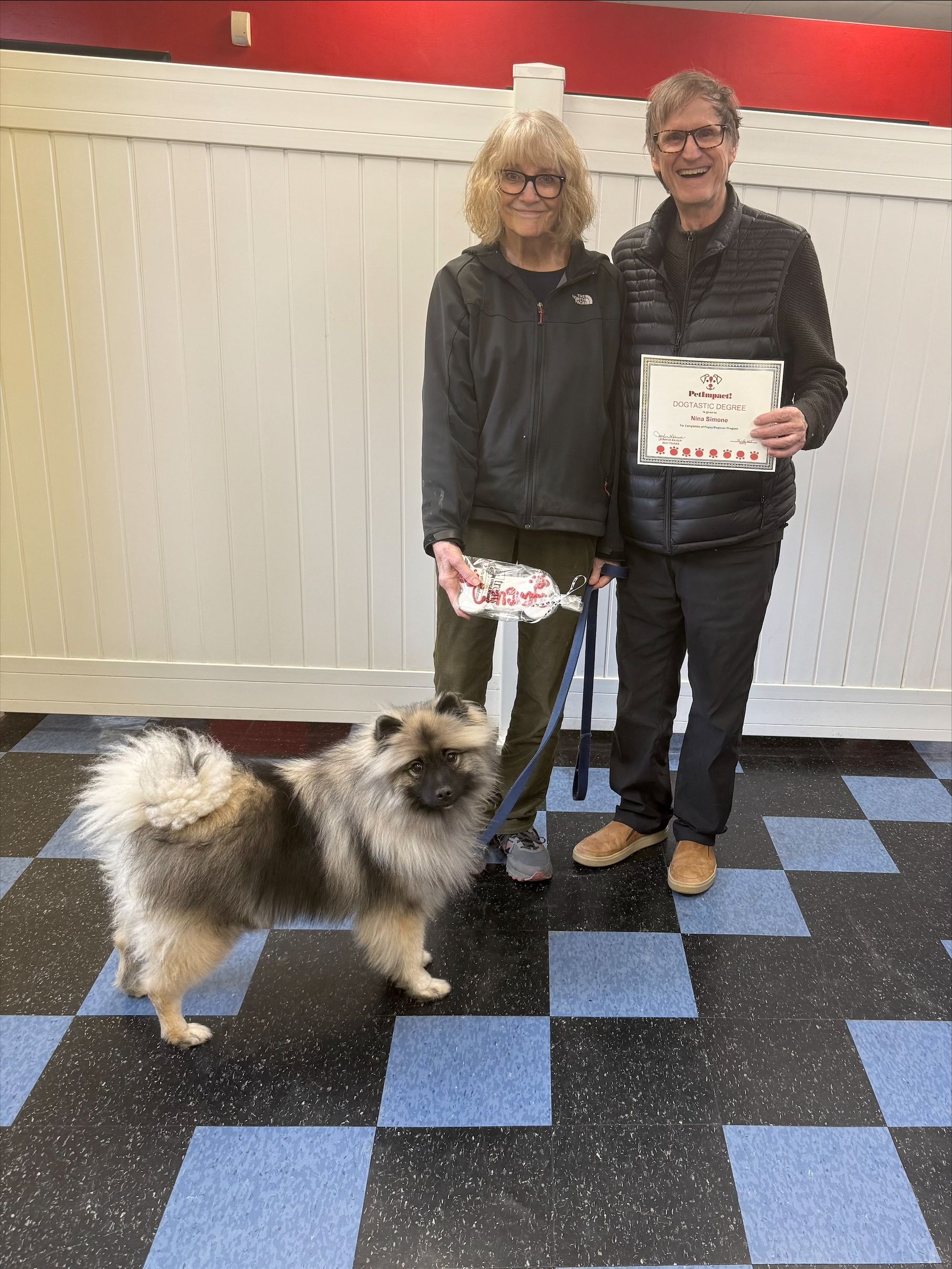 A man and a woman are standing next to a small dog and holding a certificate.