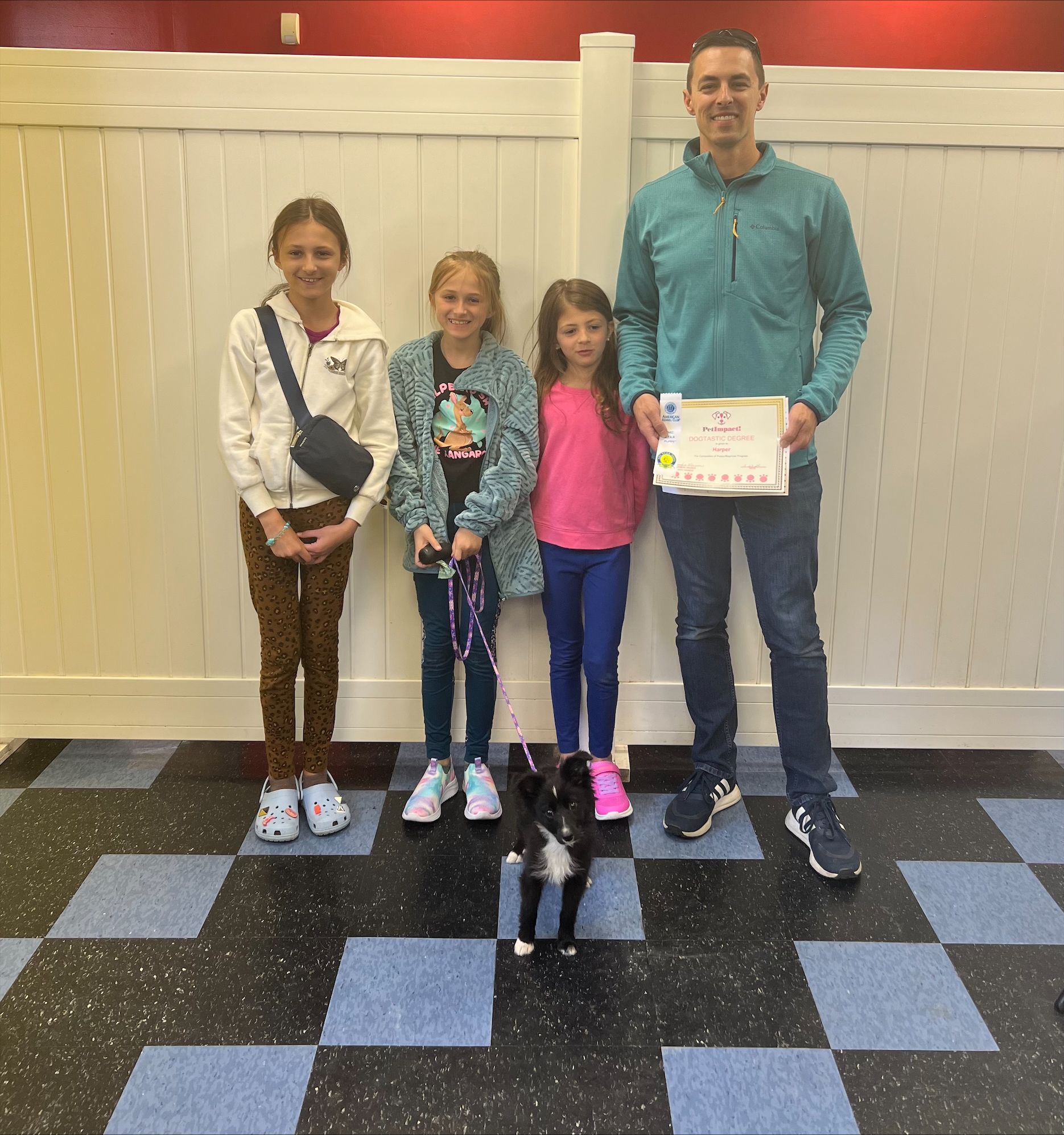 A man and three girls standing next to a black and white cat