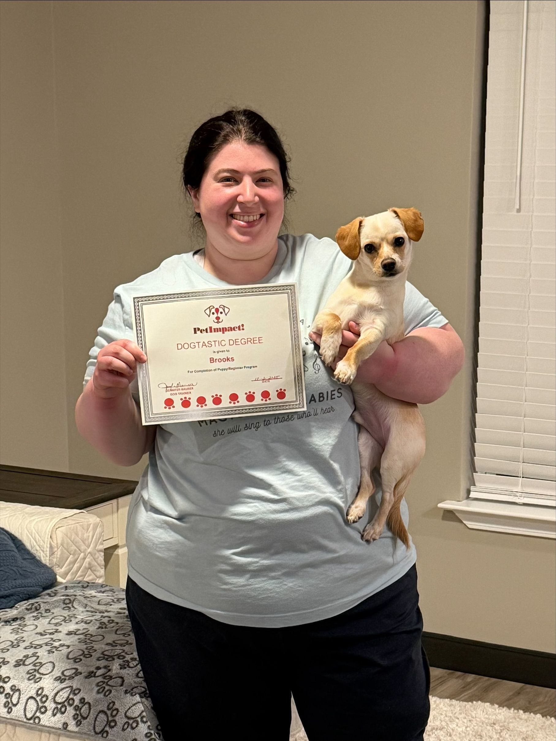 Woman holding a small dog, smiling, displaying a certificate indoors.