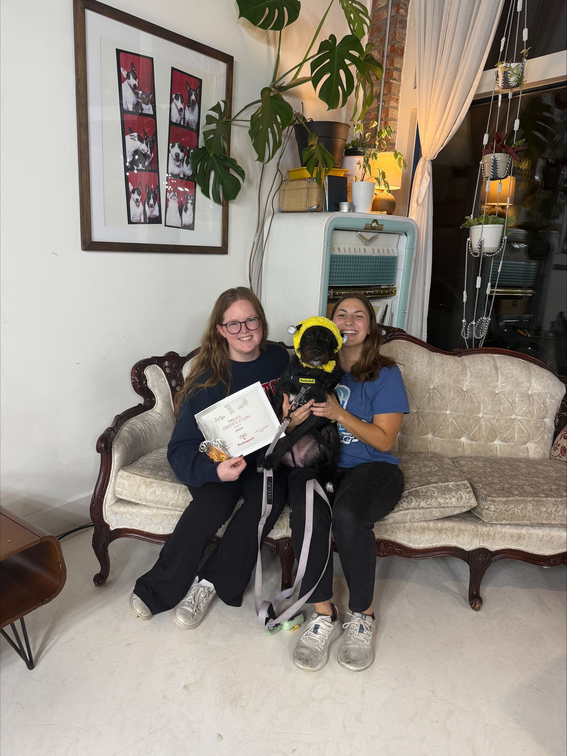 Two people seated with a dog on an ornate couch, holding a framed piece of art.