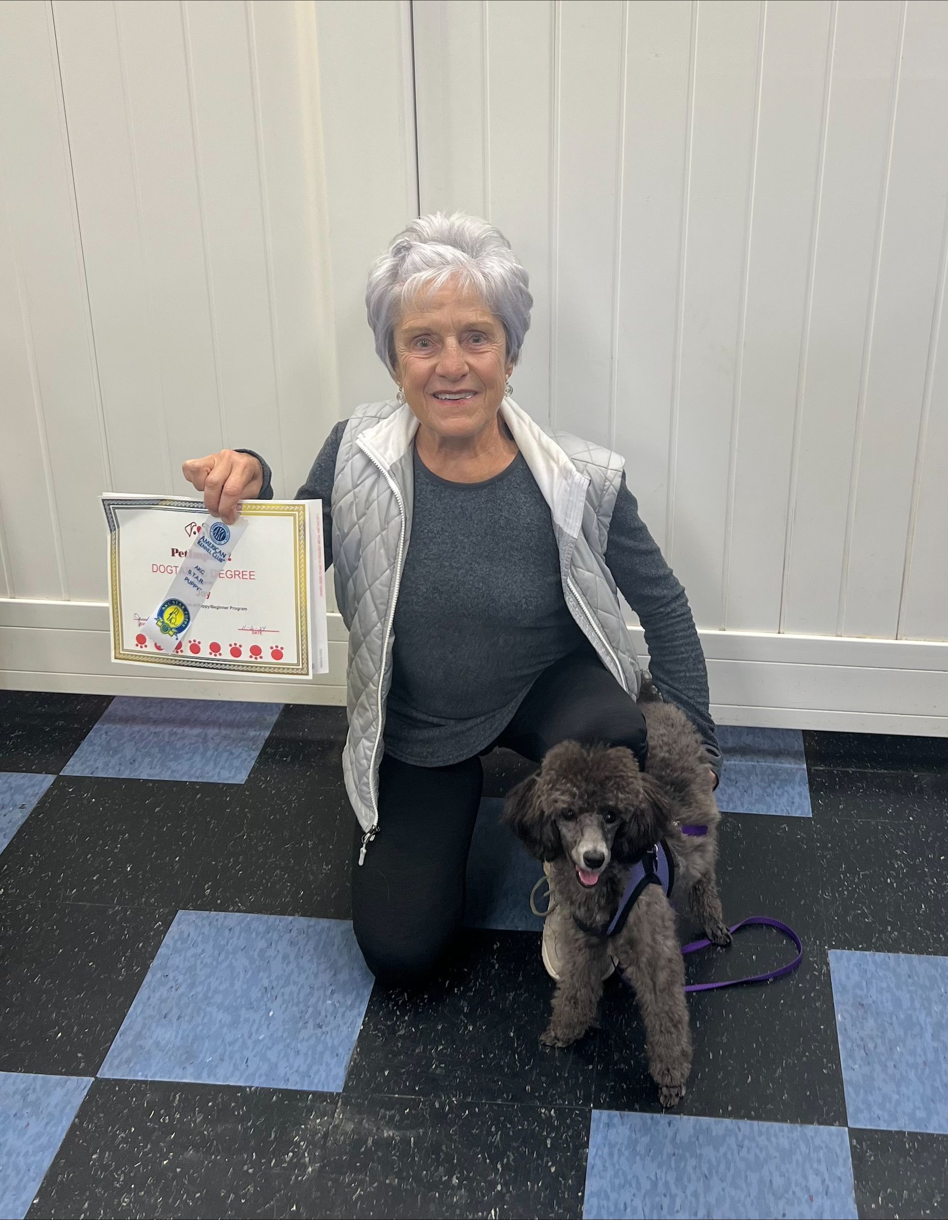A Woman Is Kneeling Down Next to A Small Poodle and Holding a Certificate.