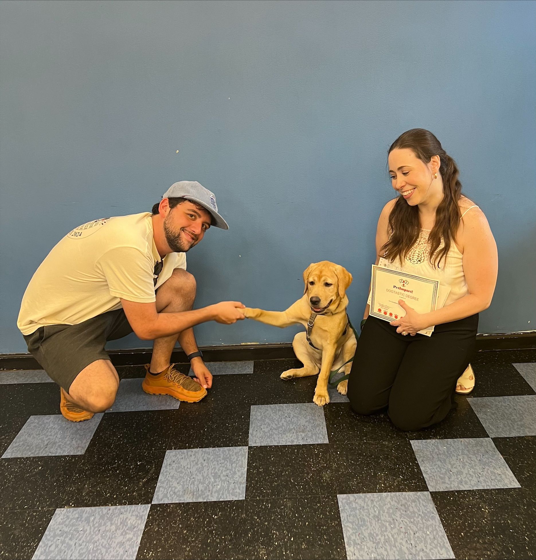 A man and woman are kneeling down next to a dog that is giving them a paw