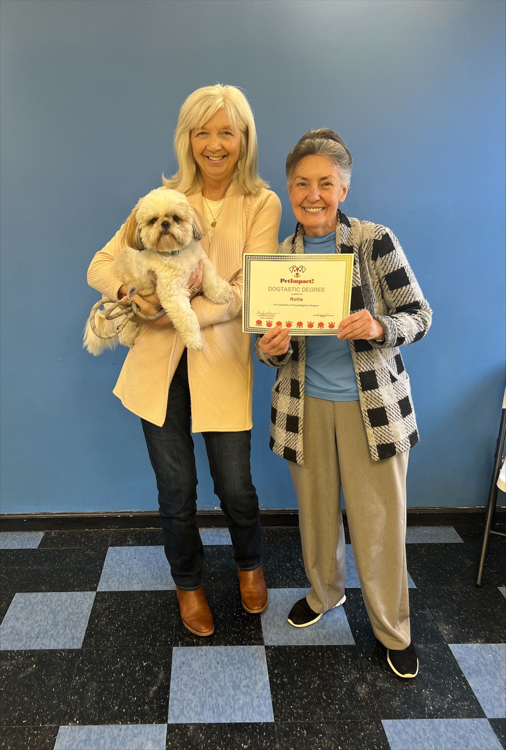 Two women are standing next to each other holding a dog and a certificate.