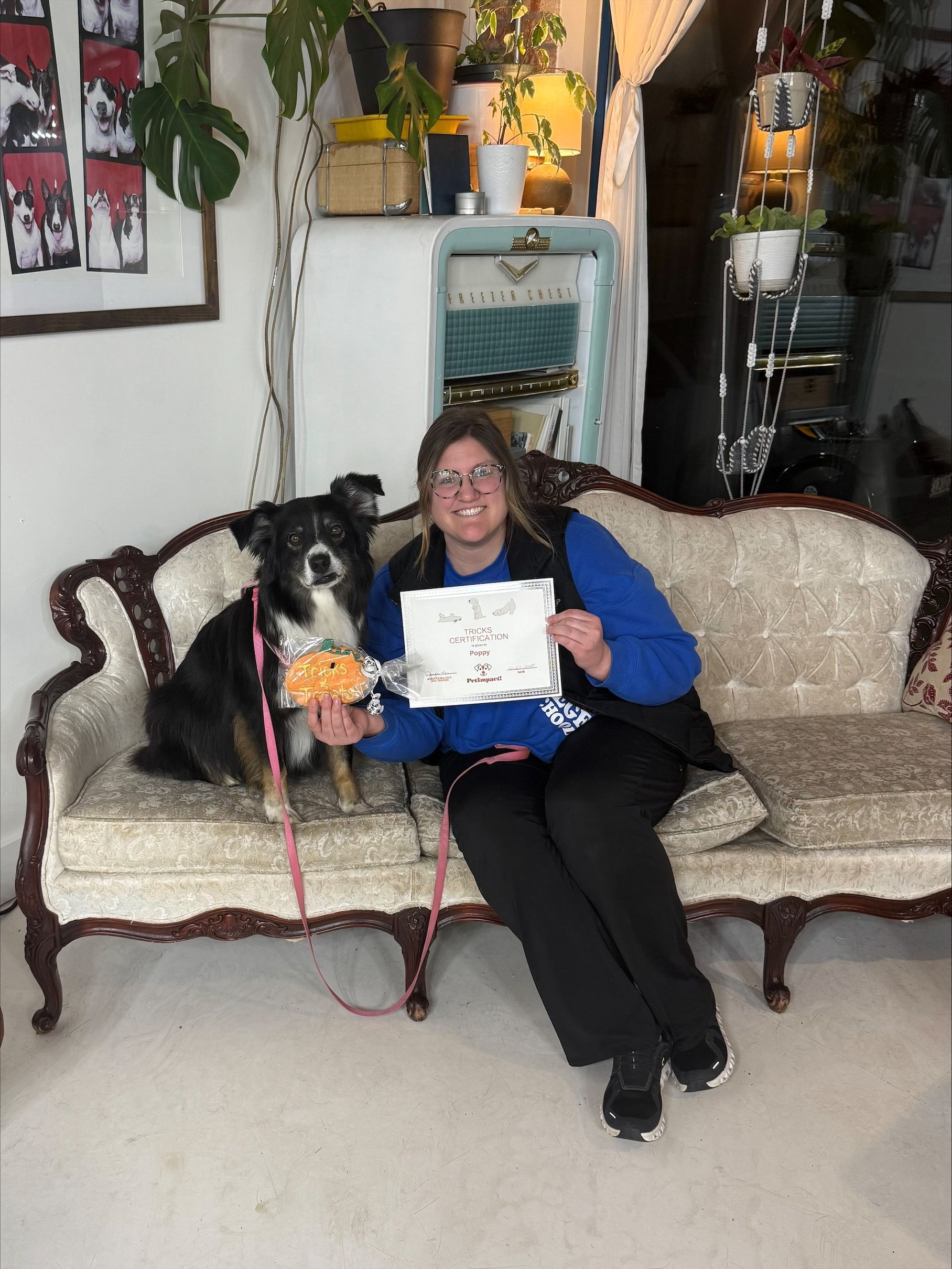 Woman and dog on ornate sofa, holding a certificate and donut, inside a shop.