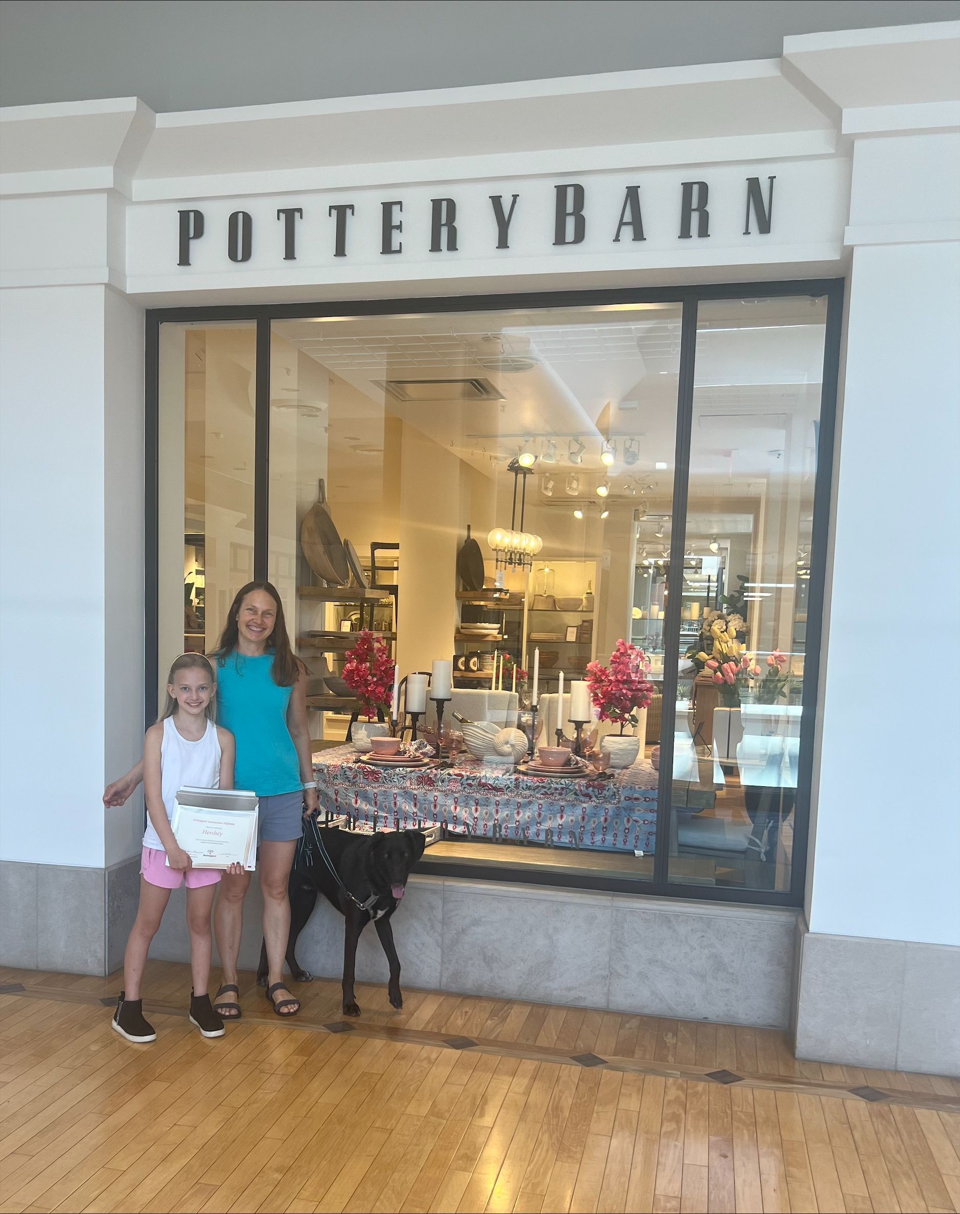 Two girls and a dog are standing in front of a pottery barn store.