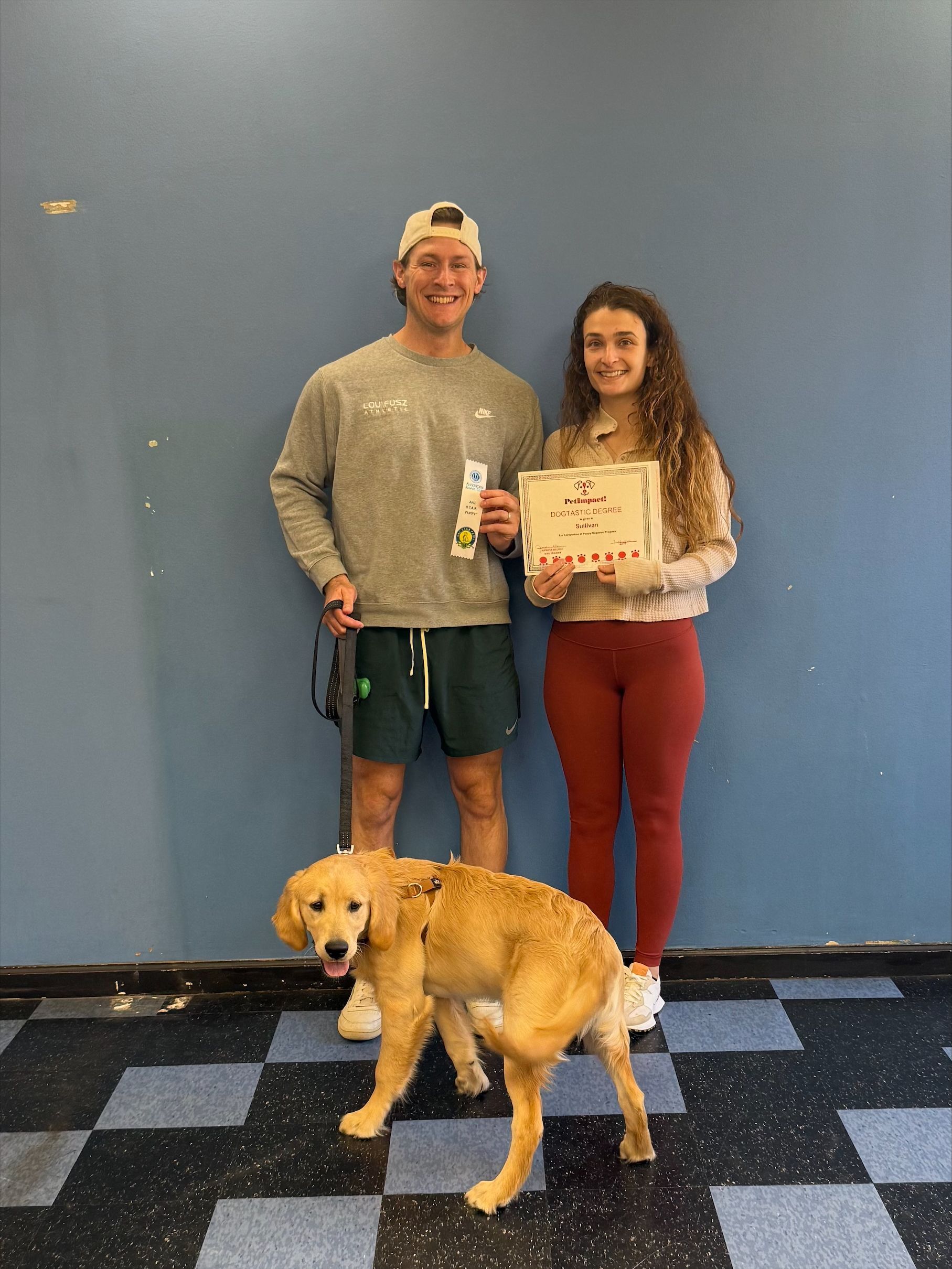 A person and a partner standing against a blue wall with a golden dog, holding a handwritten sign.