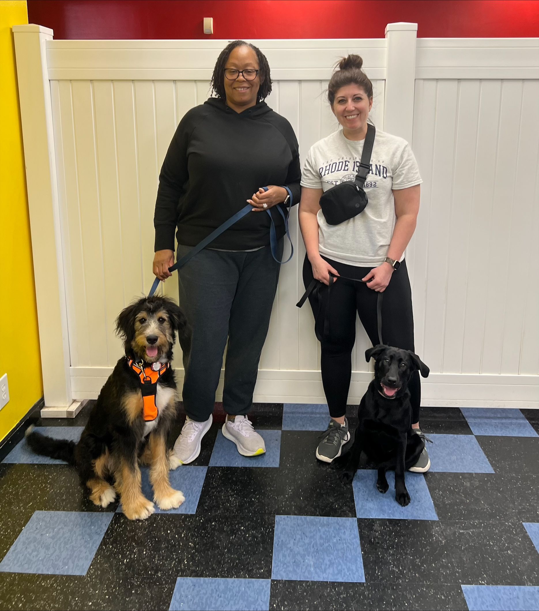 Two women standing next to two dogs in a room