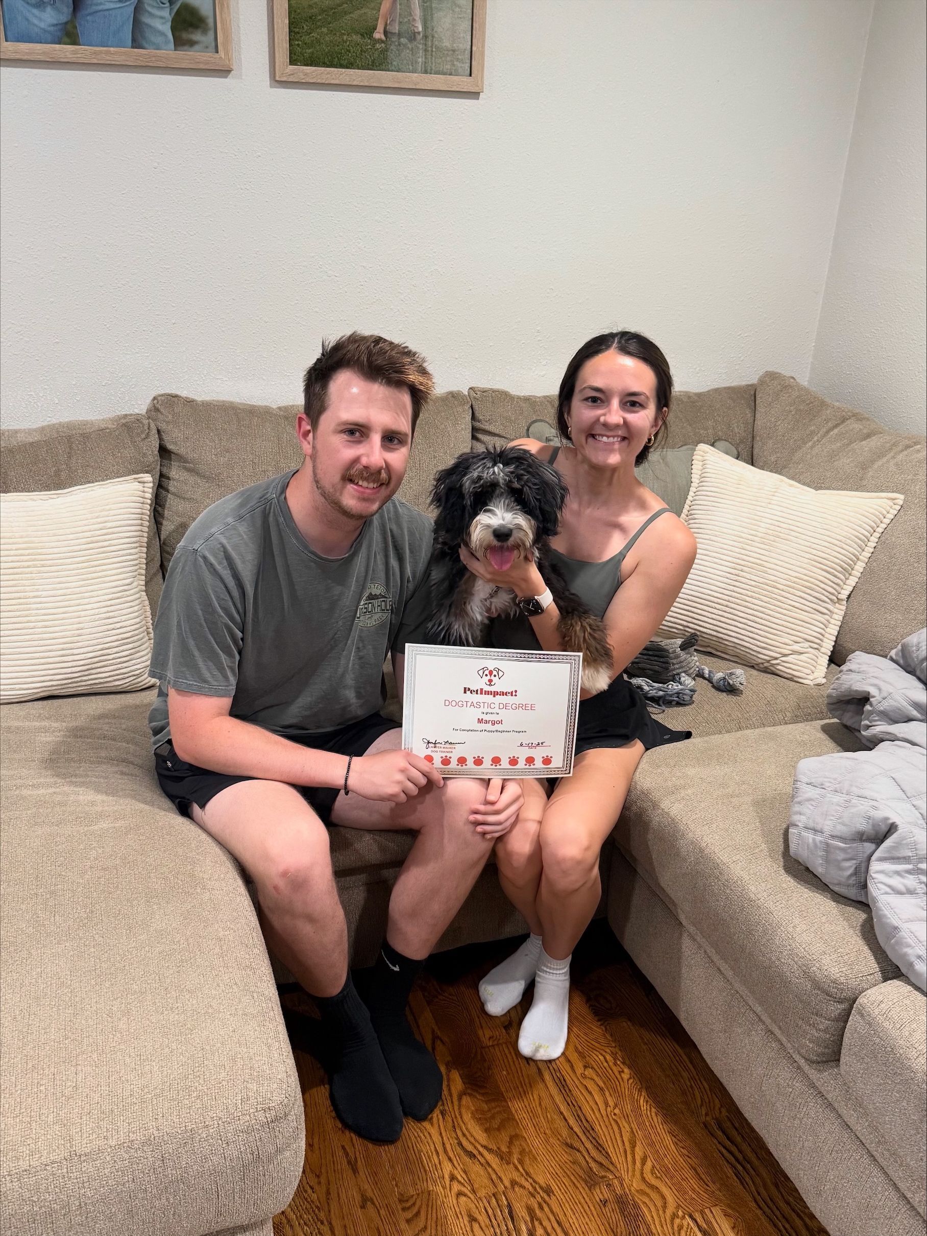 Couple on couch with dog, holding sign. Sign says 