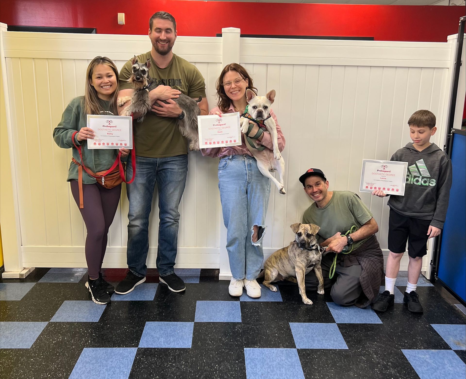 People and dogs pose, holding certificates, in a dog training setting.