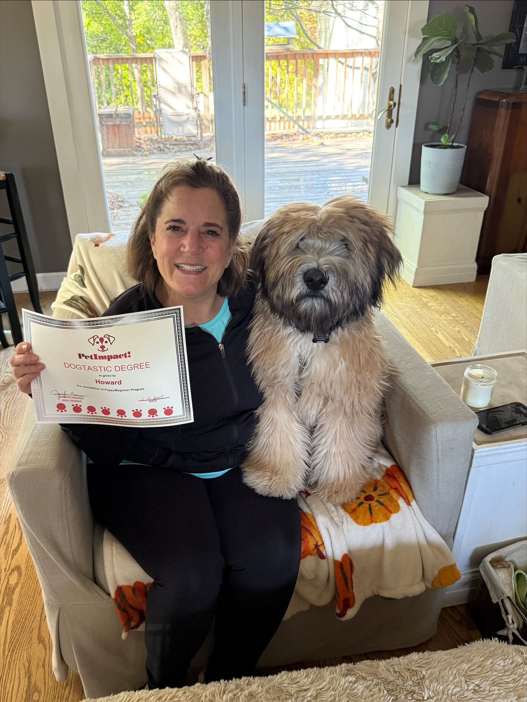 Woman and fluffy dog seated, holding framed certificate indoors.